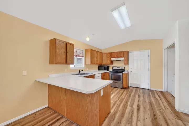 Kitchen featuring a peninsula, light countertops, stainless steel electric stove, light wood-style floors, and vaulted ceiling