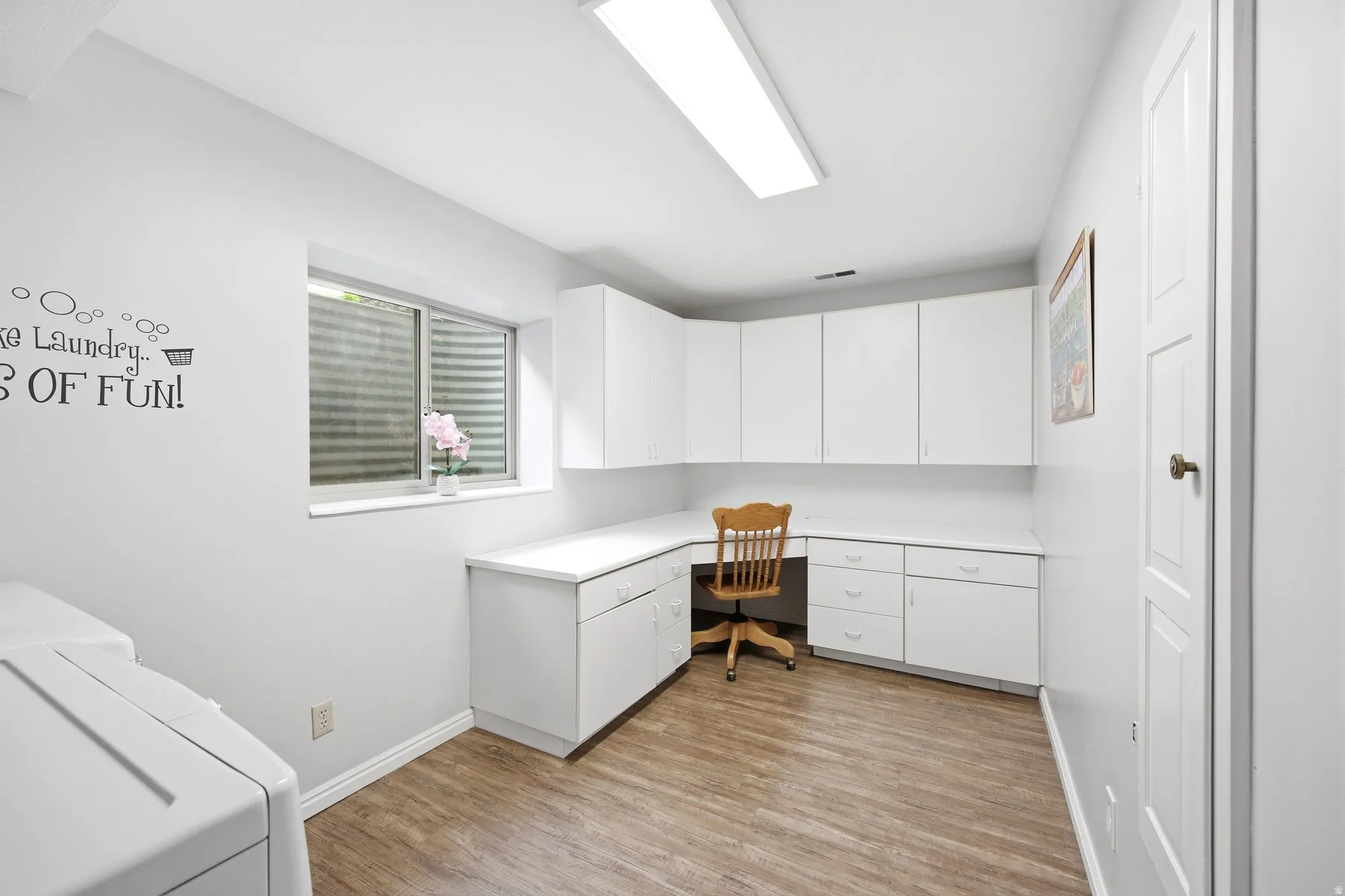 Large basement laundry room  featuring built in desk/work area, cabinetry, fold down cabinet ironing board, washer and  dryer