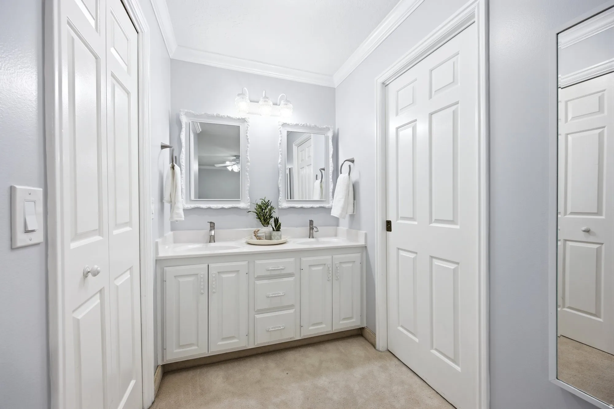 Full bath featuring a closet, double vanity, crown molding, and light carpet