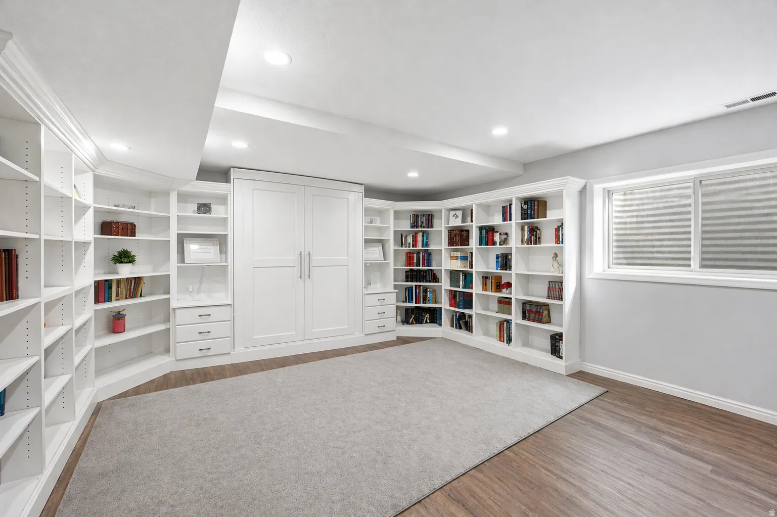 Studio apartment library/bedroom, murphy bed with light wood flooring and recessed lighting