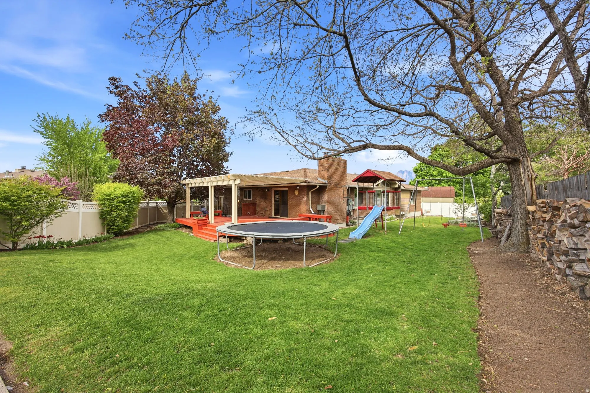 Fenced backyard with a trampoline, a playground, a deck, and a pergola