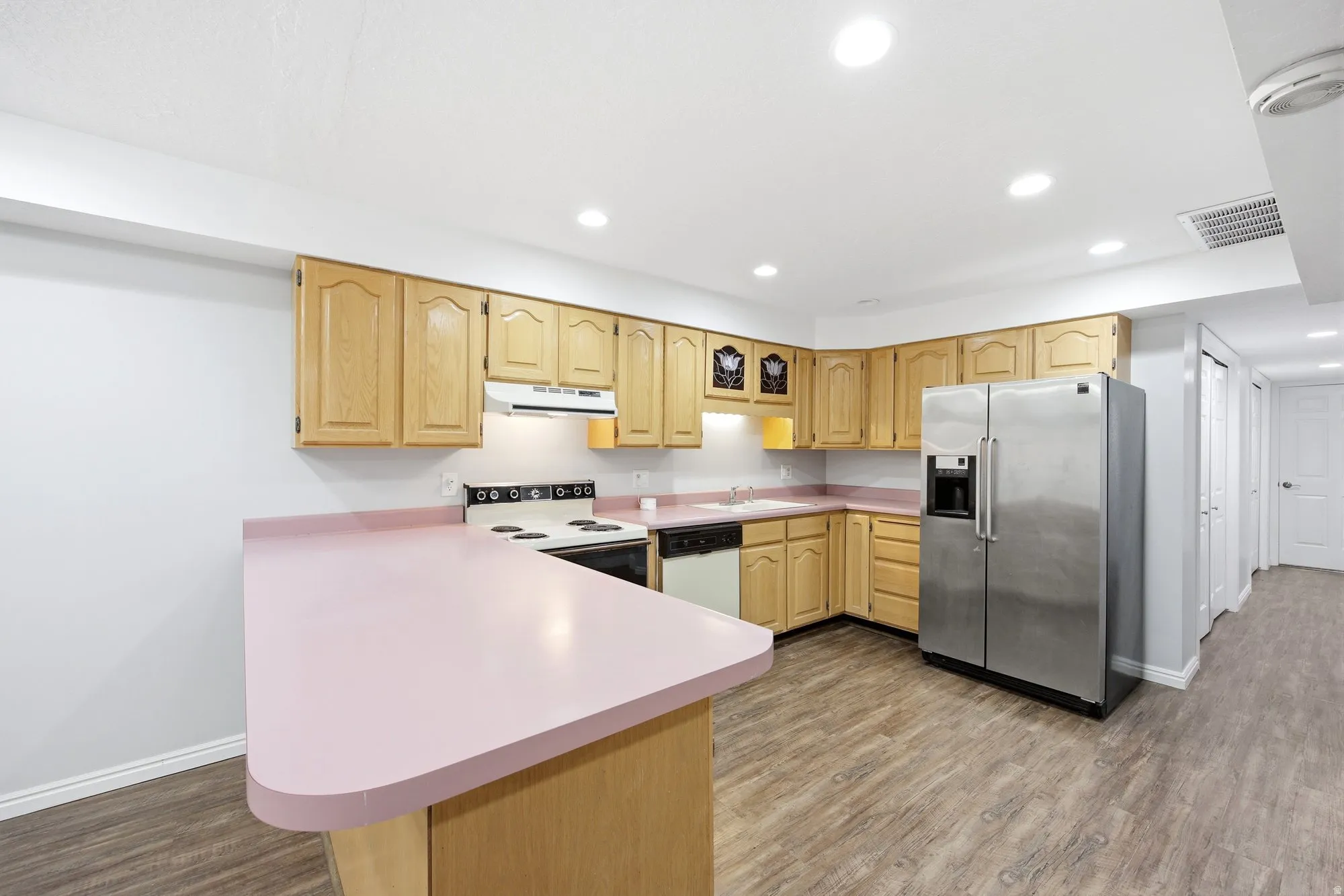 Studio apartment full kitchen featuring white and stainless appliances, light wood finish cabinets, light countertops, light wood-type flooring, and recessed lighting
