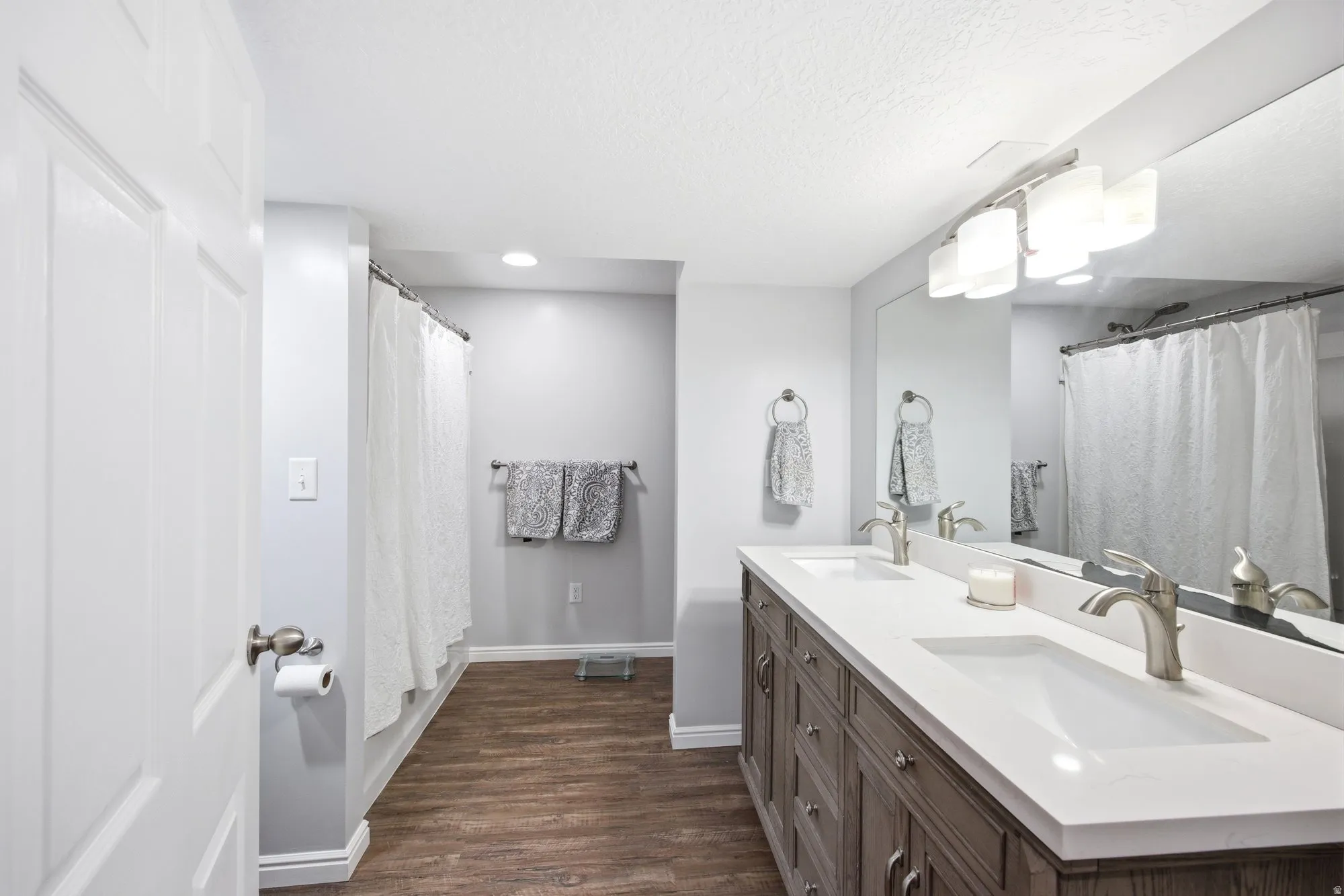 Studio apartment full bathroom featuring double vanity, a shower with curtain, tons of shelving, dark wood-style flooring, and recessed lighting, washer dryer hookups