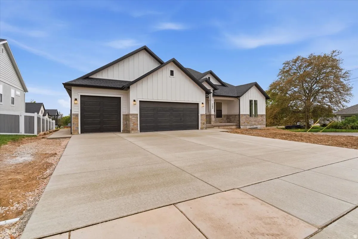 Modern farmhouse style home featuring board and batten siding, a garage, concrete driveway, and stone siding