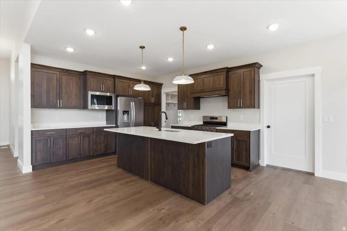 Kitchen with stainless steel appliances, dark wood-style flooring, pendant lighting, an island with sink, and dark wood finish cabinetry