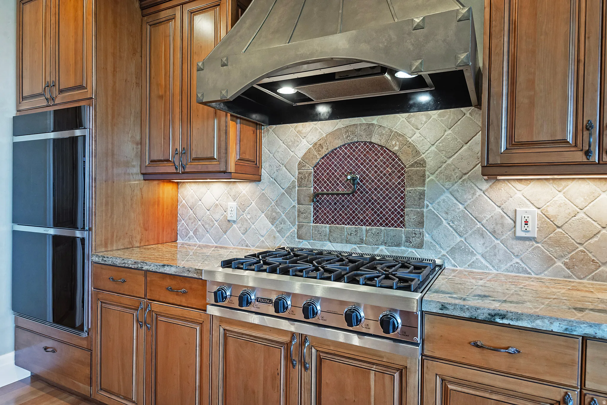 Kitchen with stainless steel gas stovetop, wood finish cabinets, decorative backsplash, and light stone counters