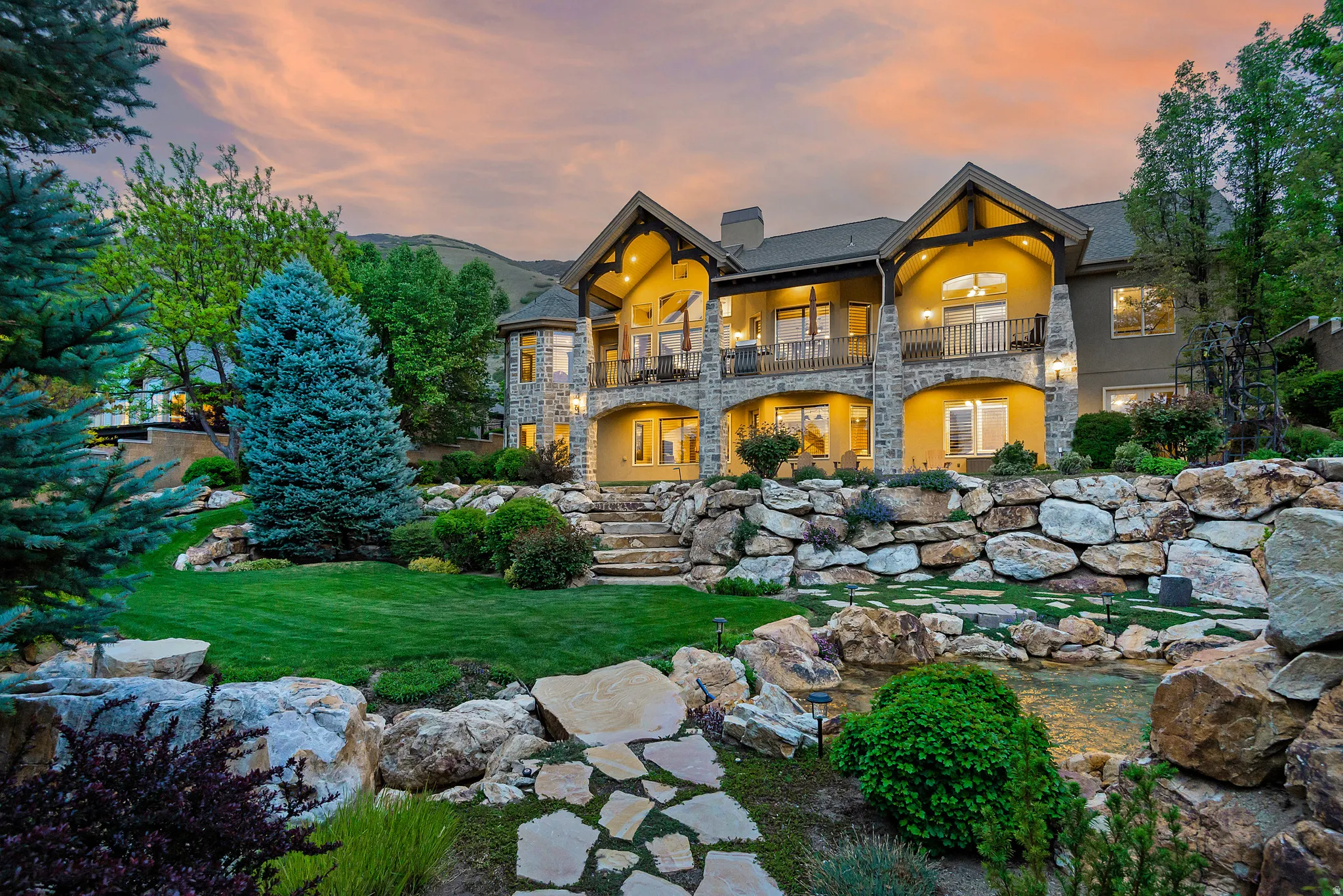 Back of property with a chimney, a balcony, a yard, a patio, and stone siding