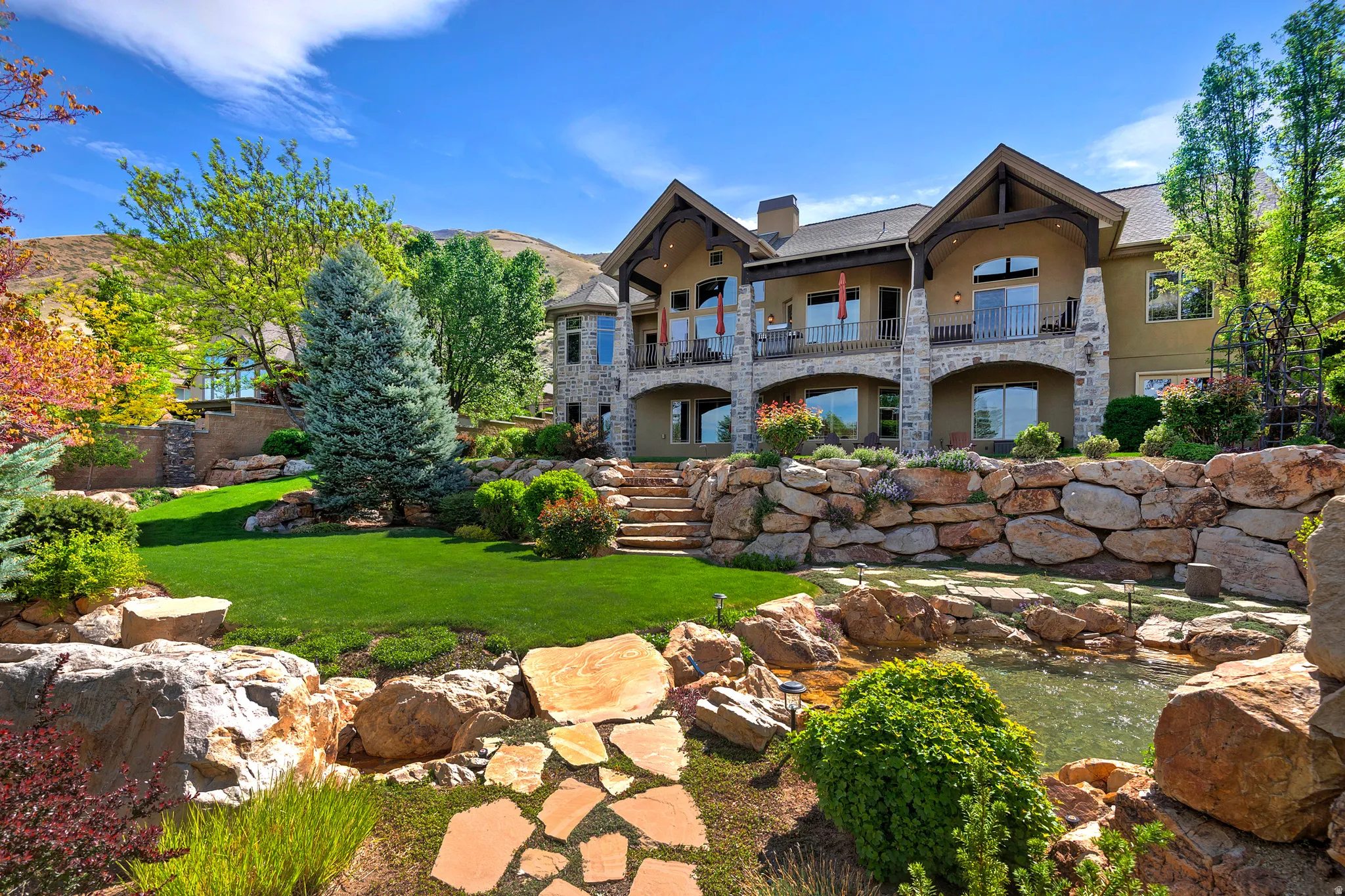 Rear view of house featuring a small pond, a chimney, a yard, stone siding, and a balcony