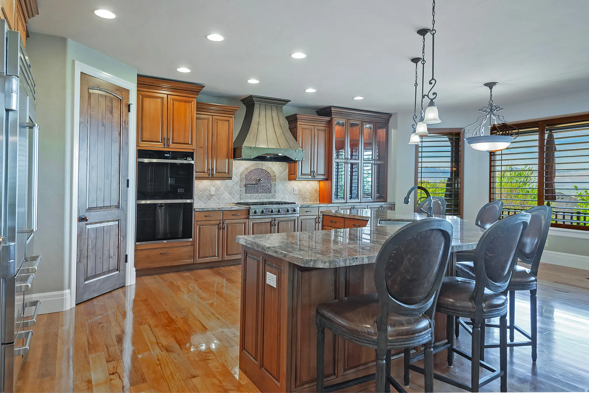 Kitchen featuring dark stone counters, stainless steel appliances, light wood finished floors, hanging light fixtures, and a kitchen bar