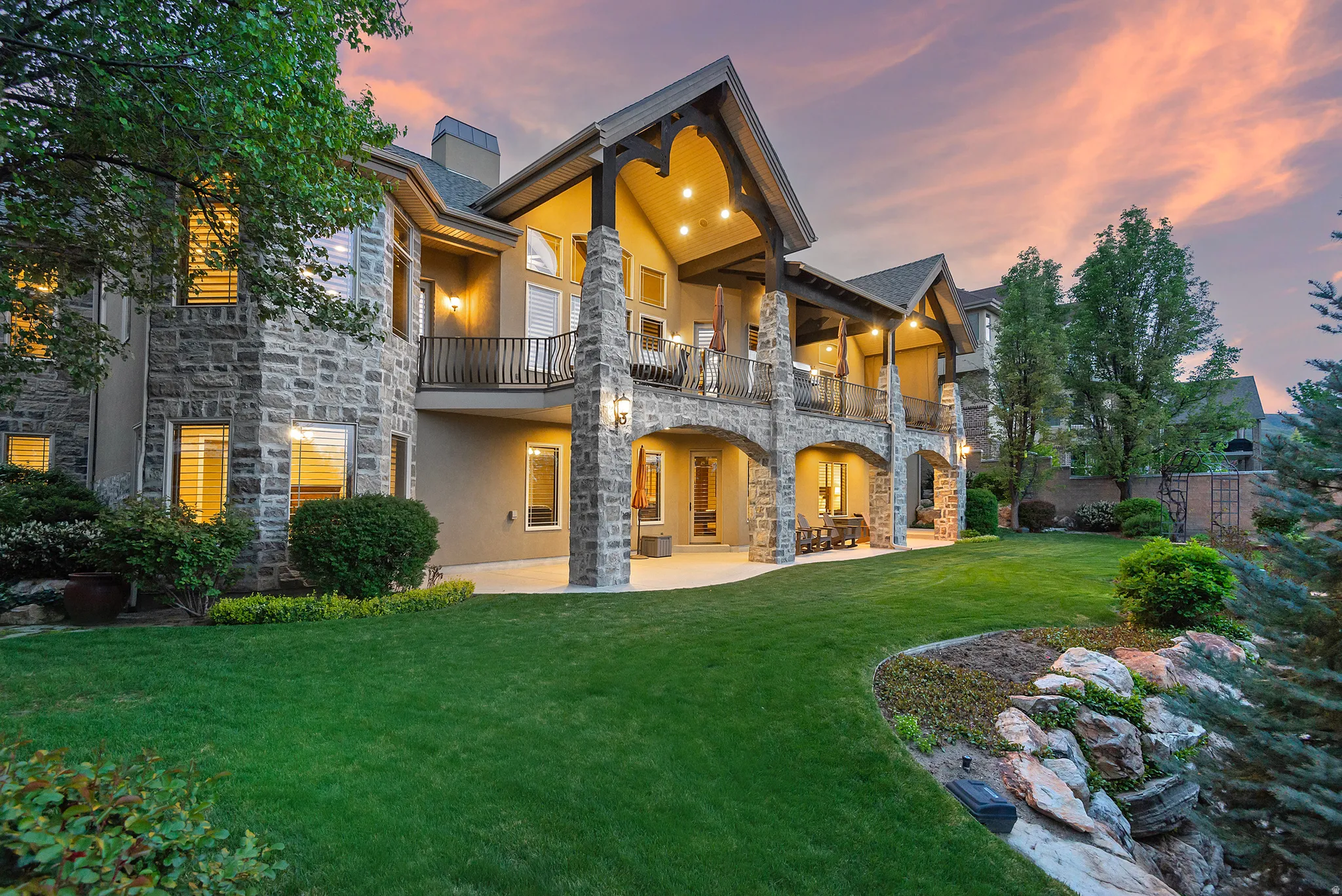 Back of property with stone siding, a lawn, a patio area, stucco siding, and a balcony