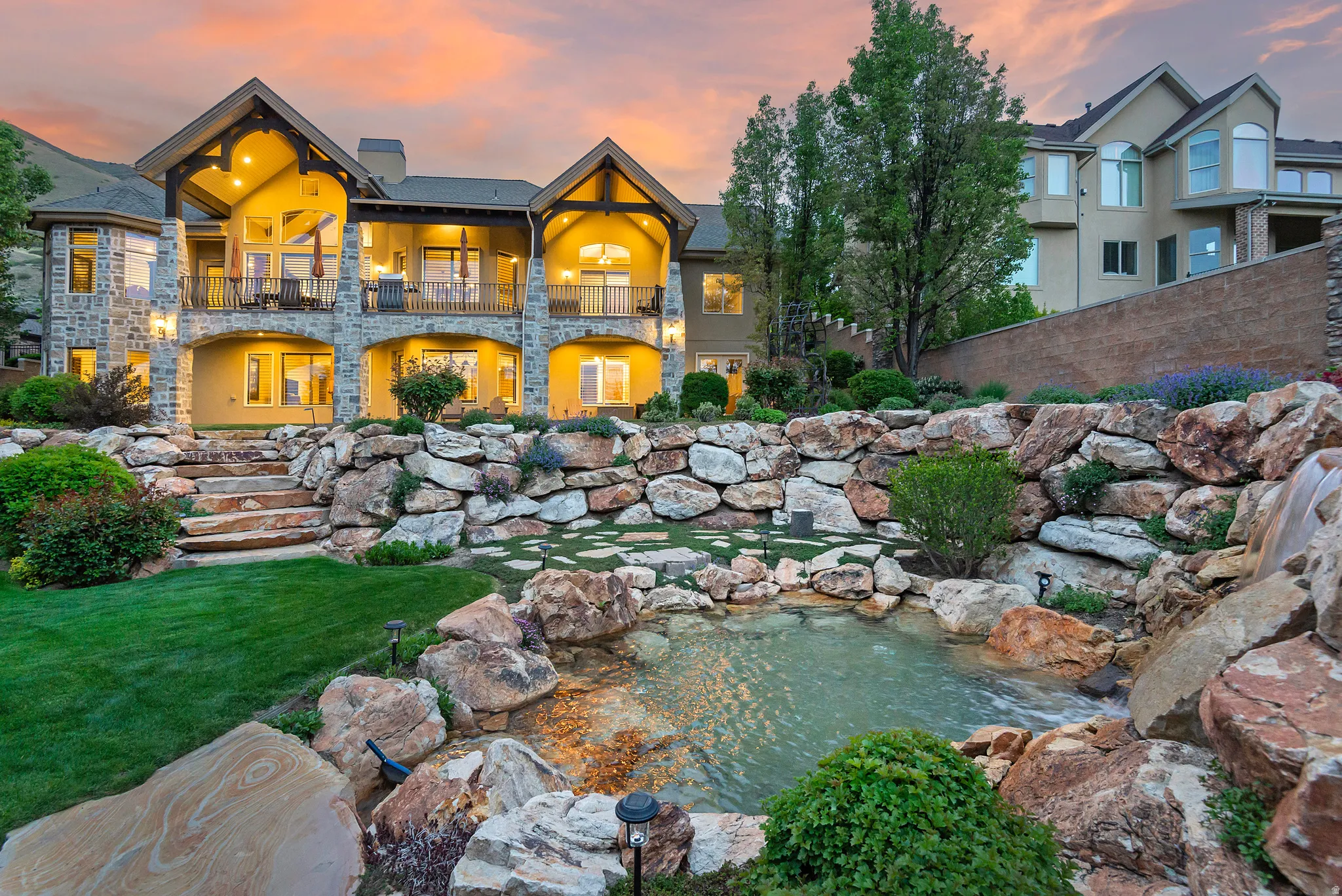 Back of property at dusk with a small pond, a balcony, a patio area, and a lawn