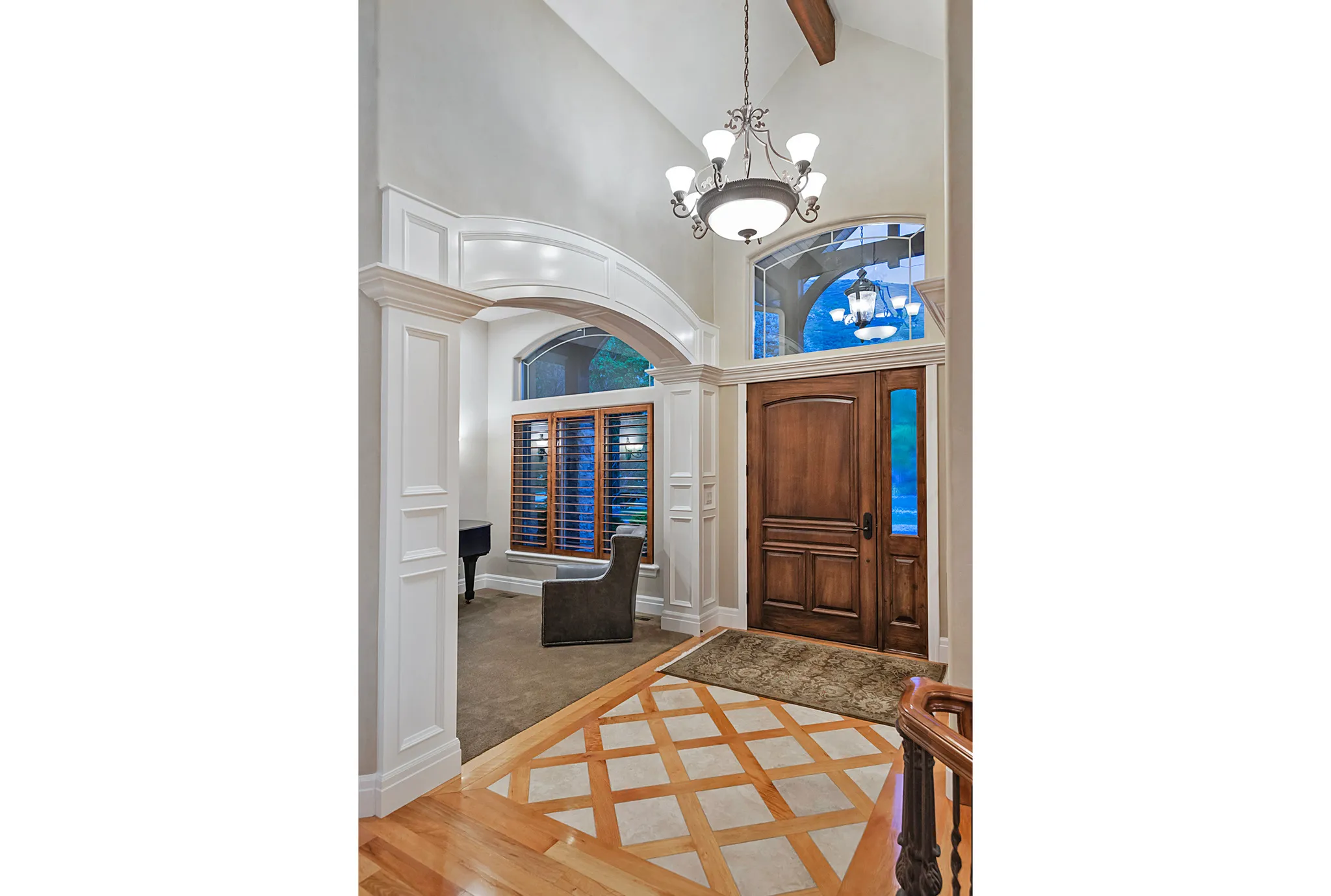 Foyer entrance featuring inlaid floor details, a chandelier, arched walkways, vaulted ceiling, and light wood-style floors