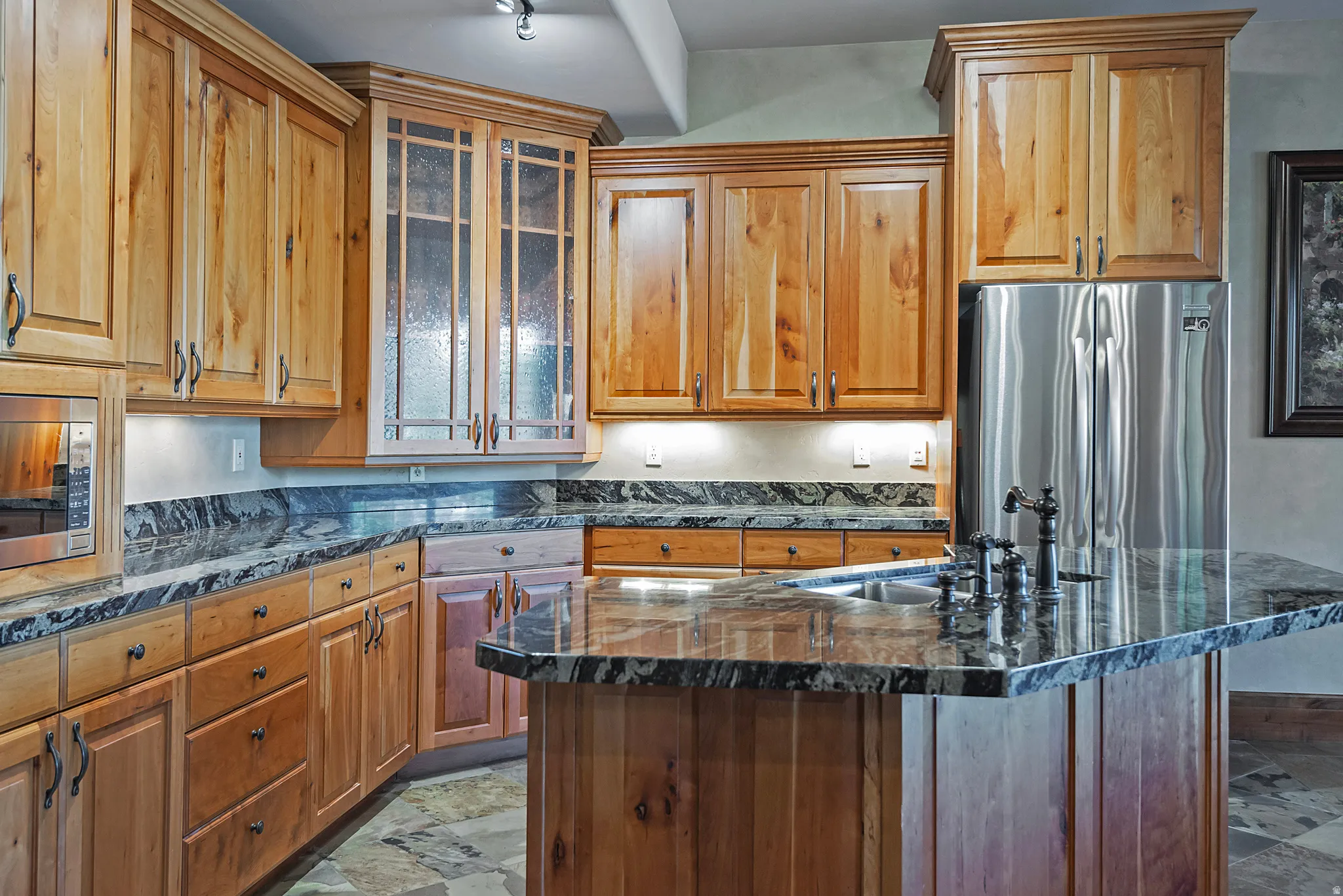 Kitchen featuring stainless steel appliances, dark stone counters, wood finish cabinets, and a kitchen island with sink