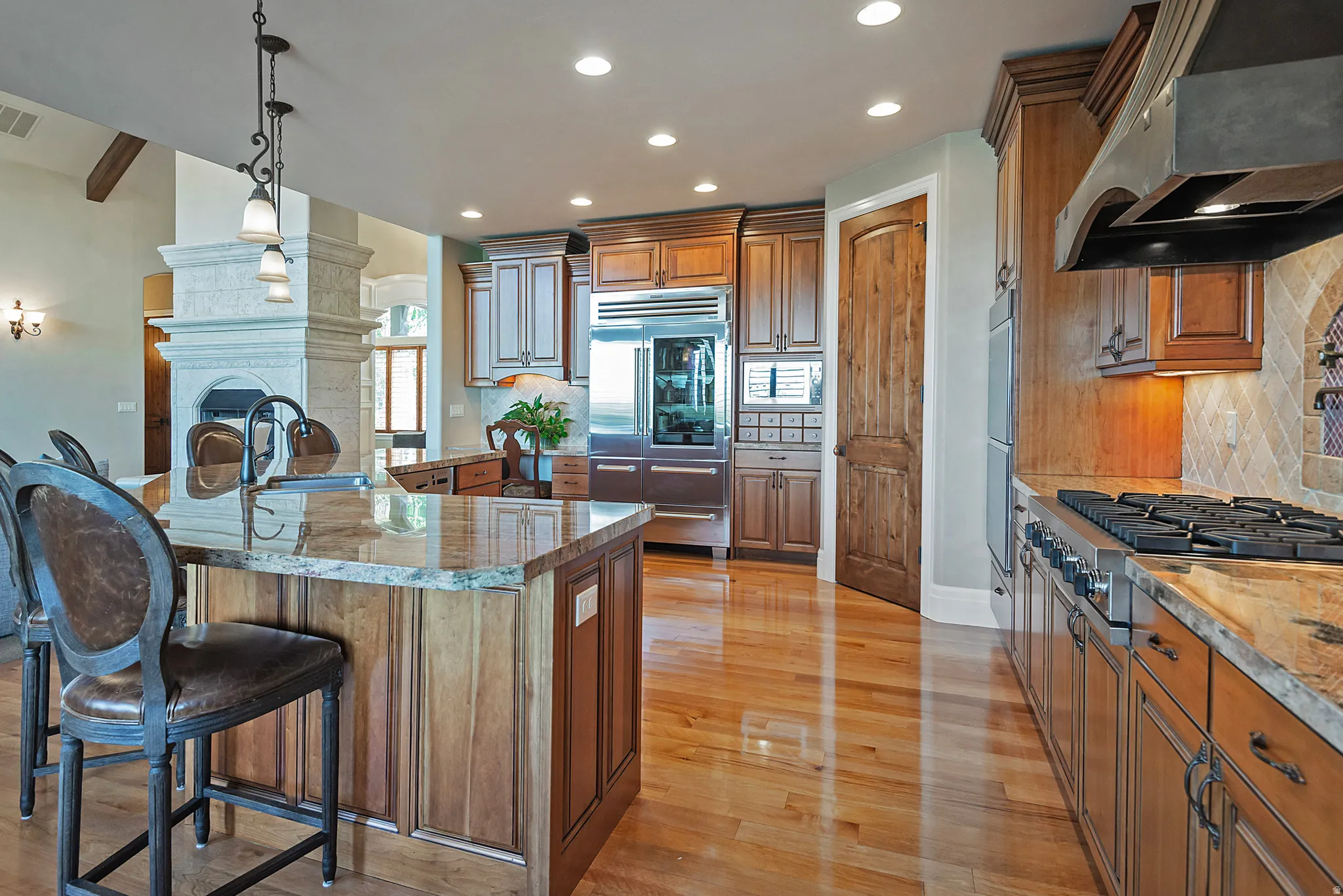 Kitchen featuring wood finish cabinetry, extractor fan, pendant lighting, light stone counters, and stainless steel appliances