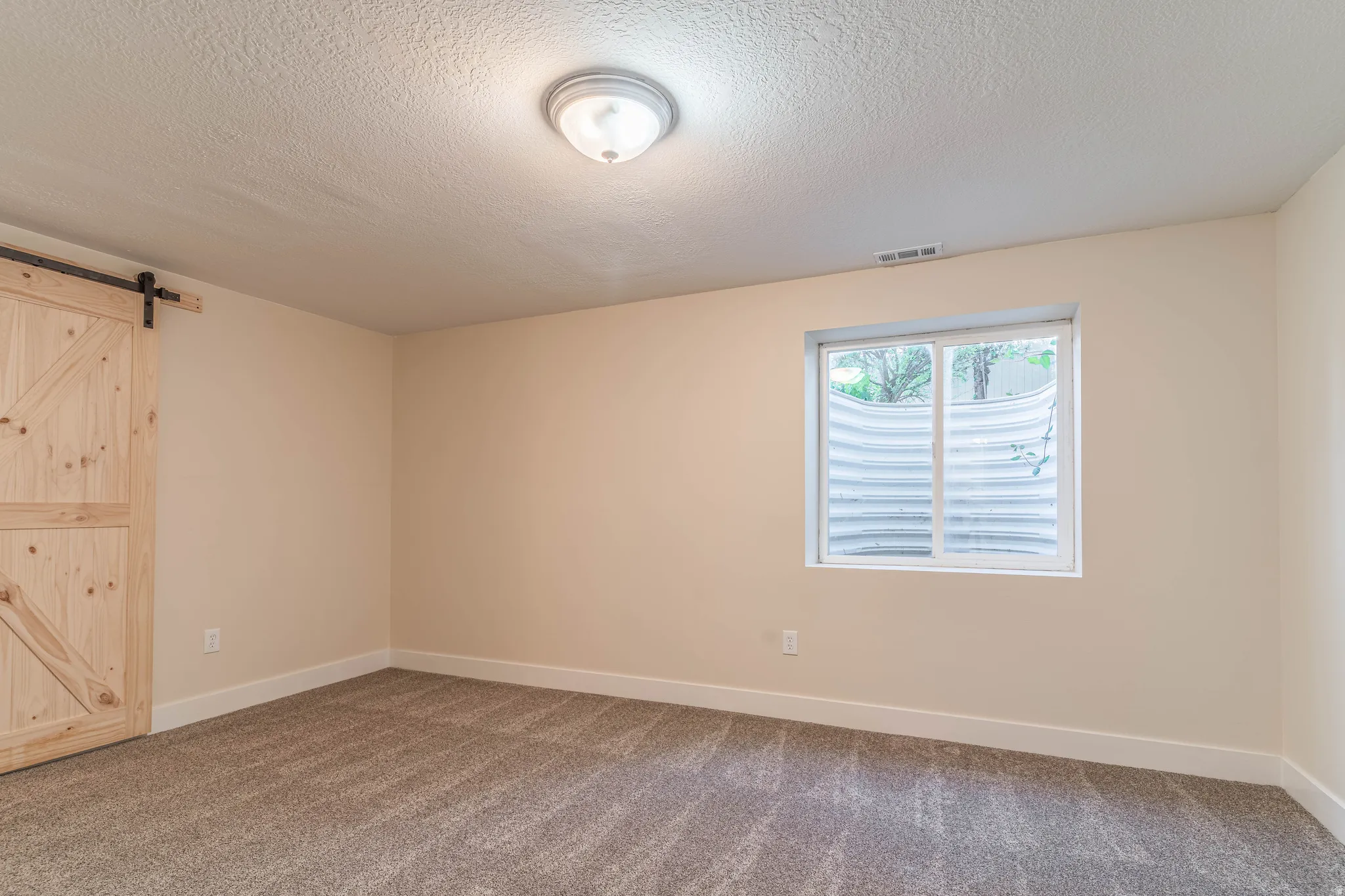 Unfurnished bedroom with a barn door, carpet flooring, and a textured ceiling