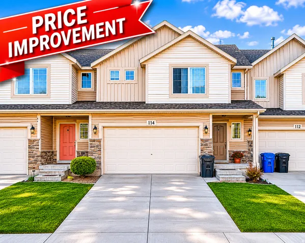 Contemporary townhome exterior featuring an attached garage, a distinct coral entry door, stacked stone accents, and a well-maintained lawn with a concrete driveway
