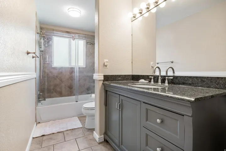 Full bath with a textured wall, vanity, shower / bath combination with glass door, and light tile patterned floors