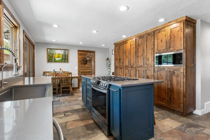 Dual tone kitchen with stainless steel appliances, dark stone finish flooring, recessed lighting, a center island, and light stone counters