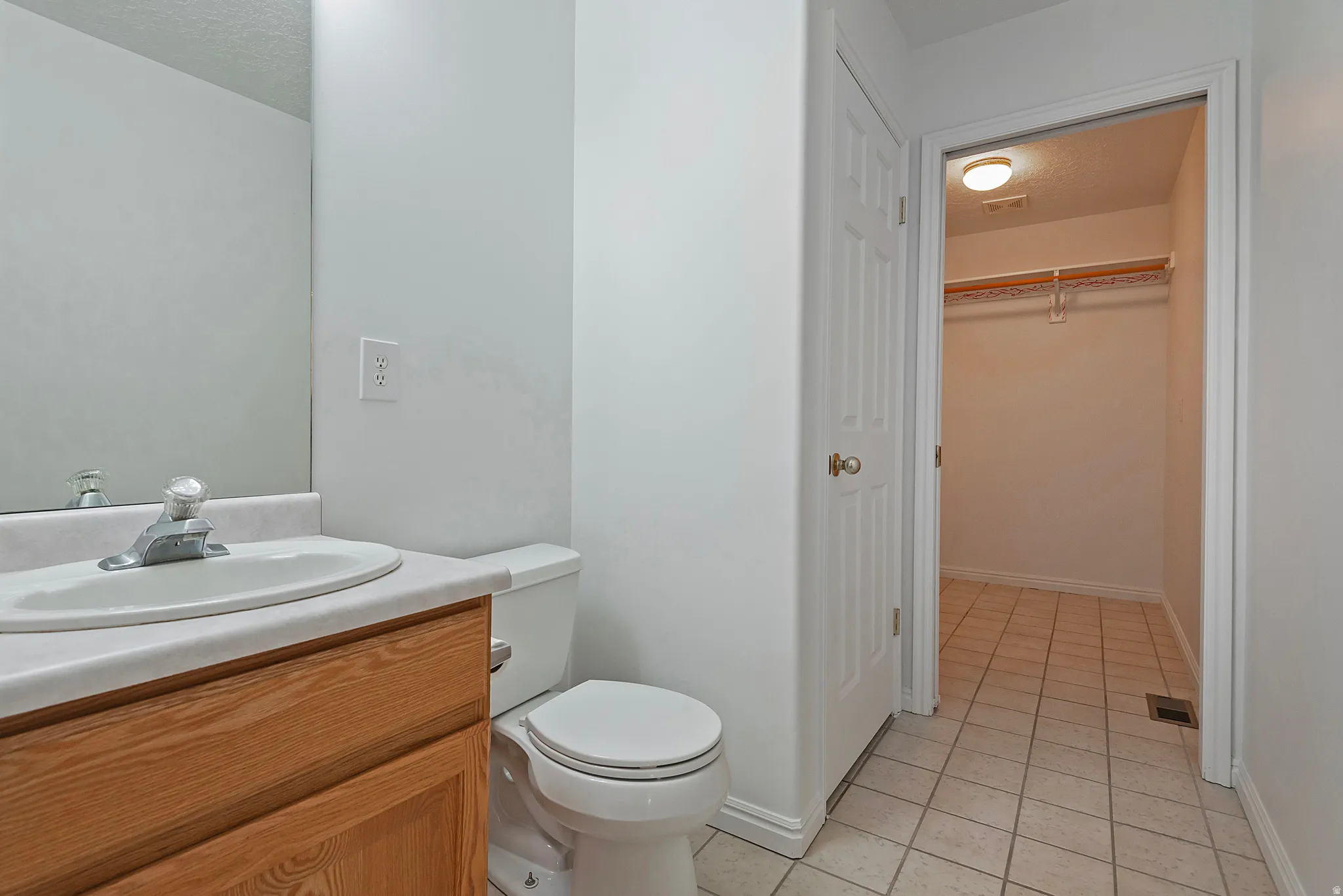 Bathroom with vanity, light tile patterned floors, a walk in closet, and a textured ceiling