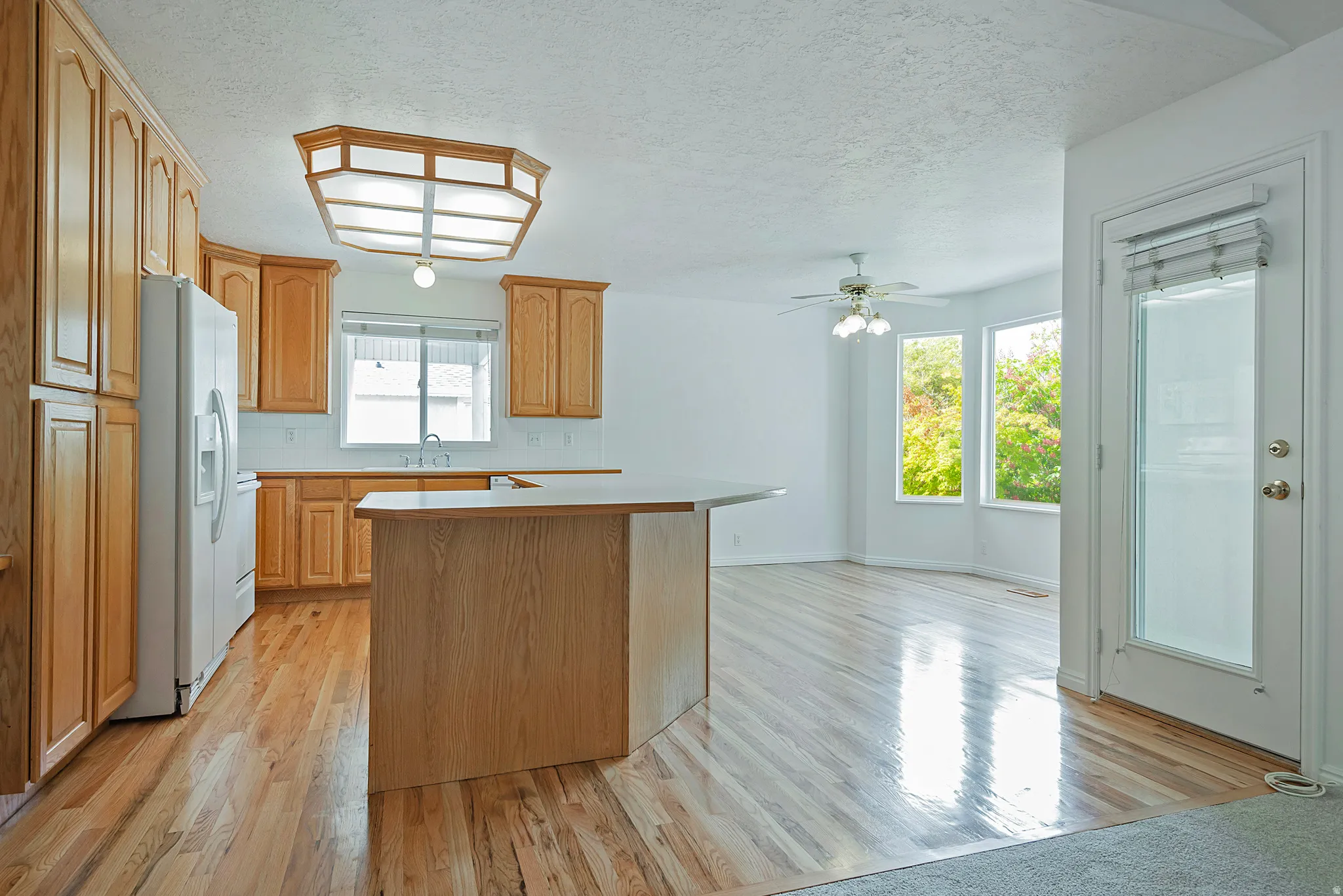 Kitchen featuring light countertops, light wood-style flooring, a textured ceiling, white appliances, and a kitchen island