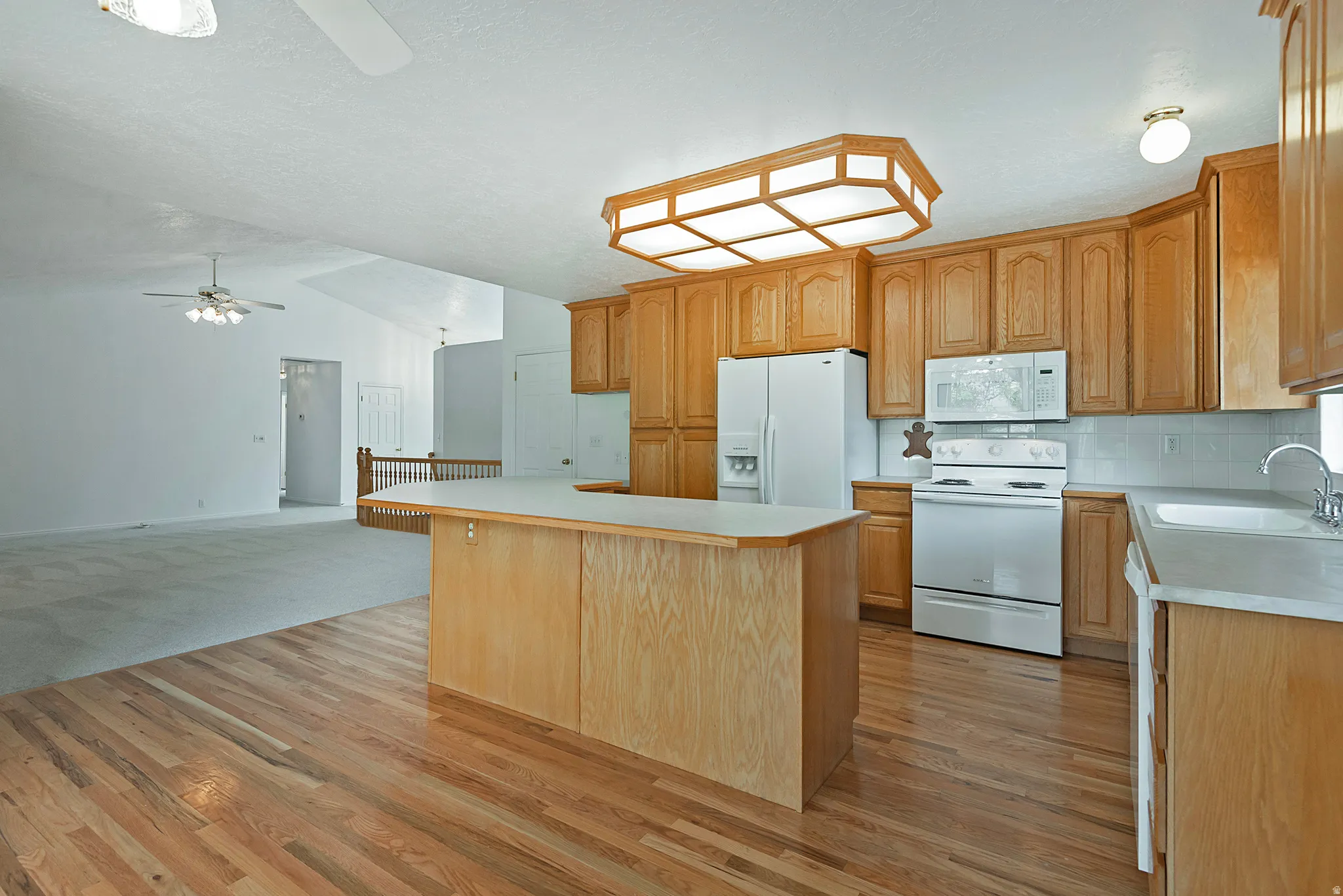Kitchen featuring ceiling fan, white appliances, light countertops, a kitchen island, and backsplash