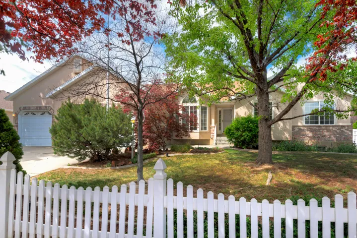 View of front facade featuring stucco siding, brick siding, an attached garage, driveway, and a fenced front yard