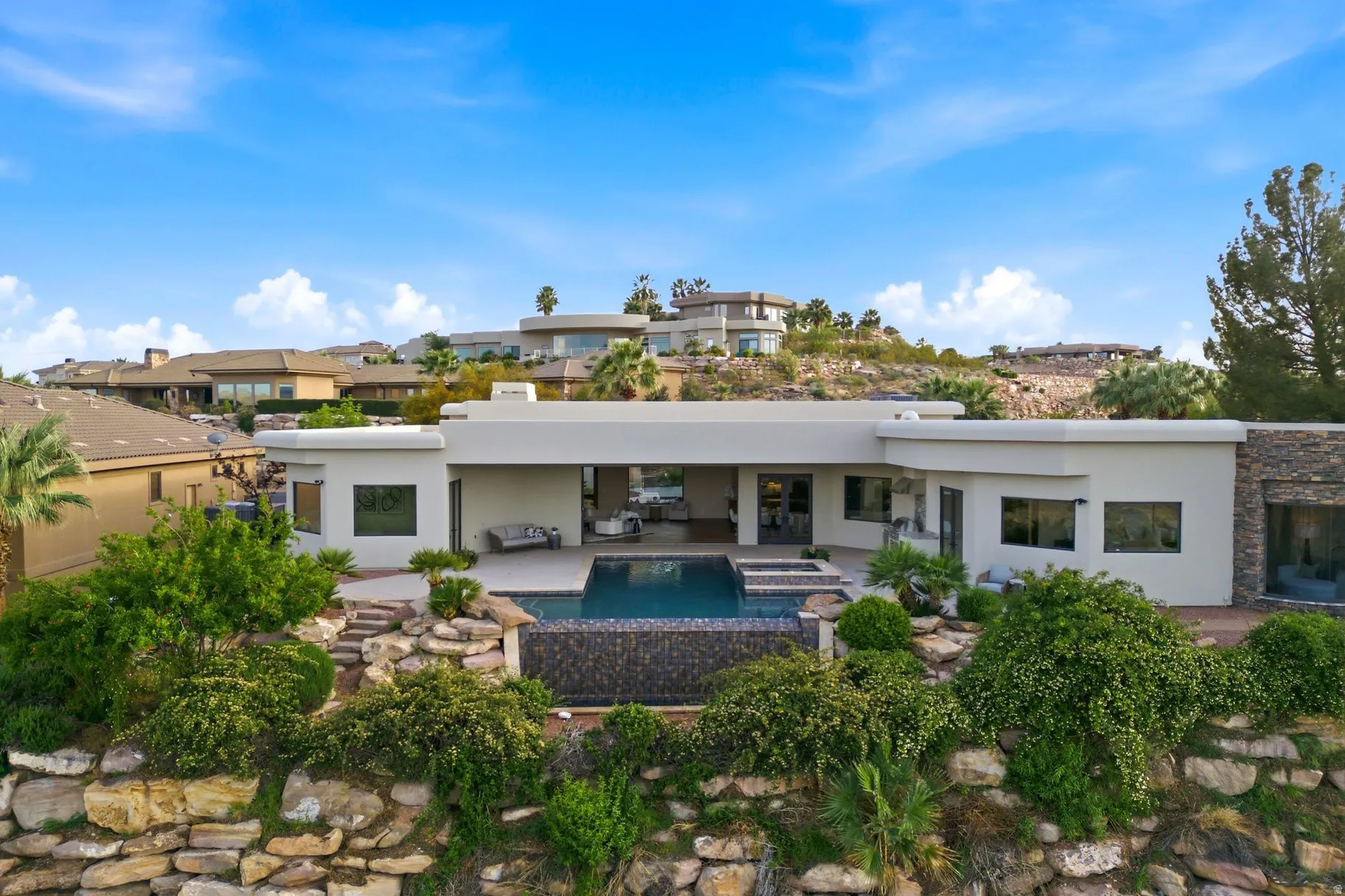 Back of property featuring stucco siding, a patio, stone siding, and a pool with connected hot tub