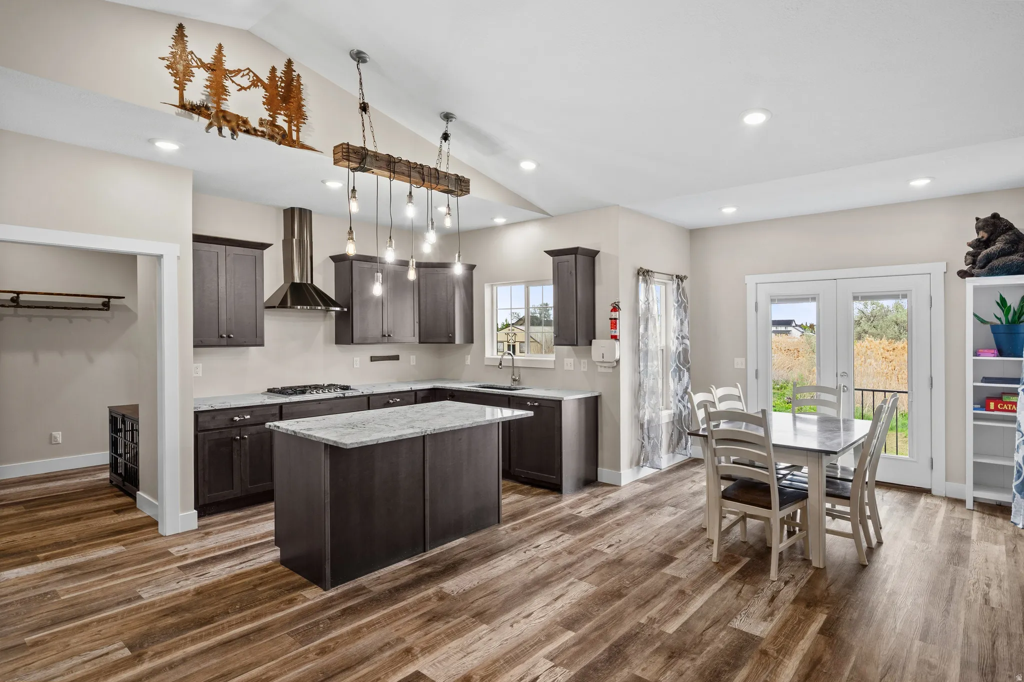 Kitchen with dark wood finish cabinets, a center island, vaulted ceiling, french doors, and light stone counters
