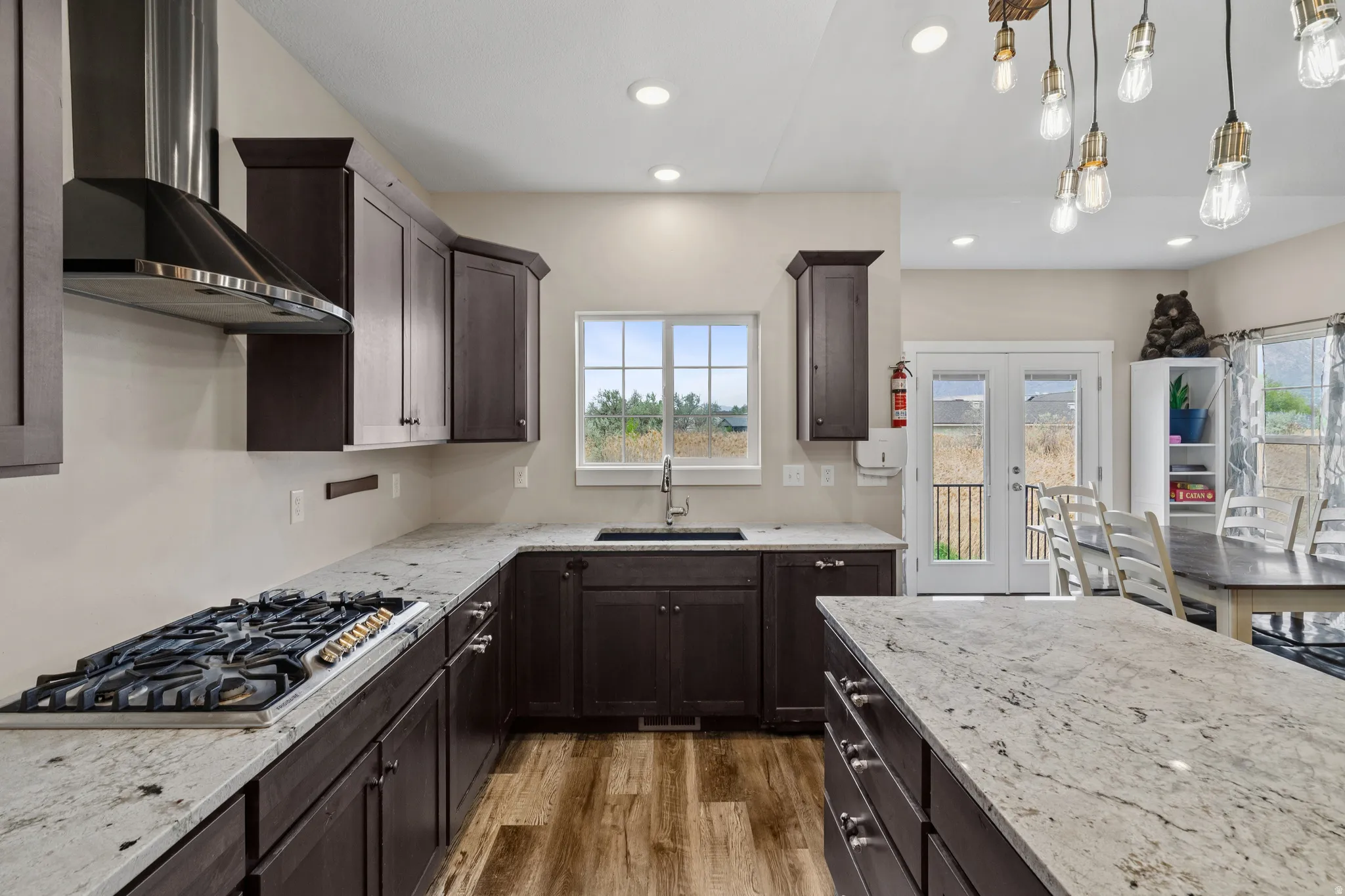 Kitchen with dark wood finish cabinets, light stone counters, stainless steel gas cooktop, and light wood-type flooring