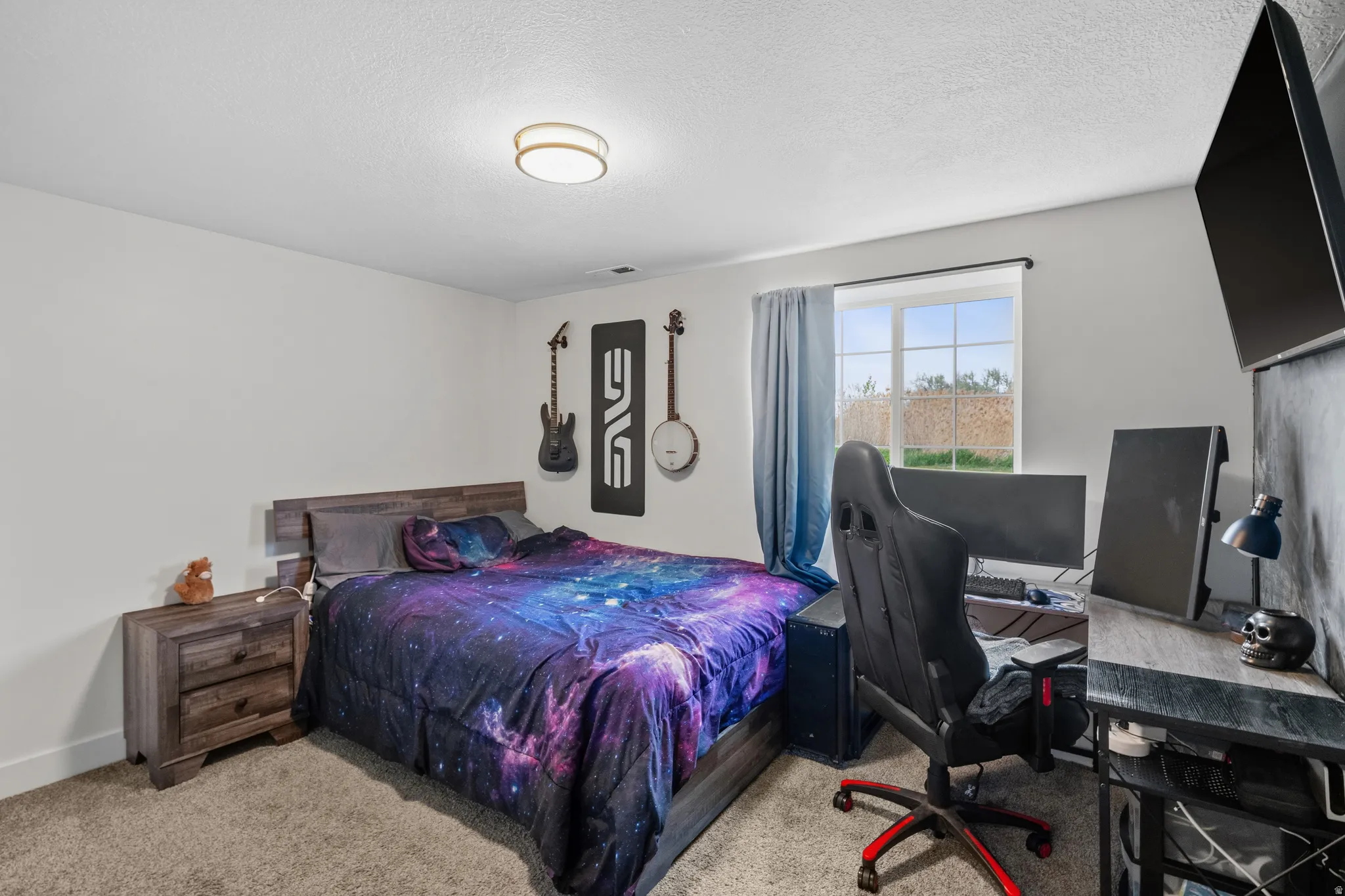 Bedroom with a desk, light colored carpet, and a textured ceiling