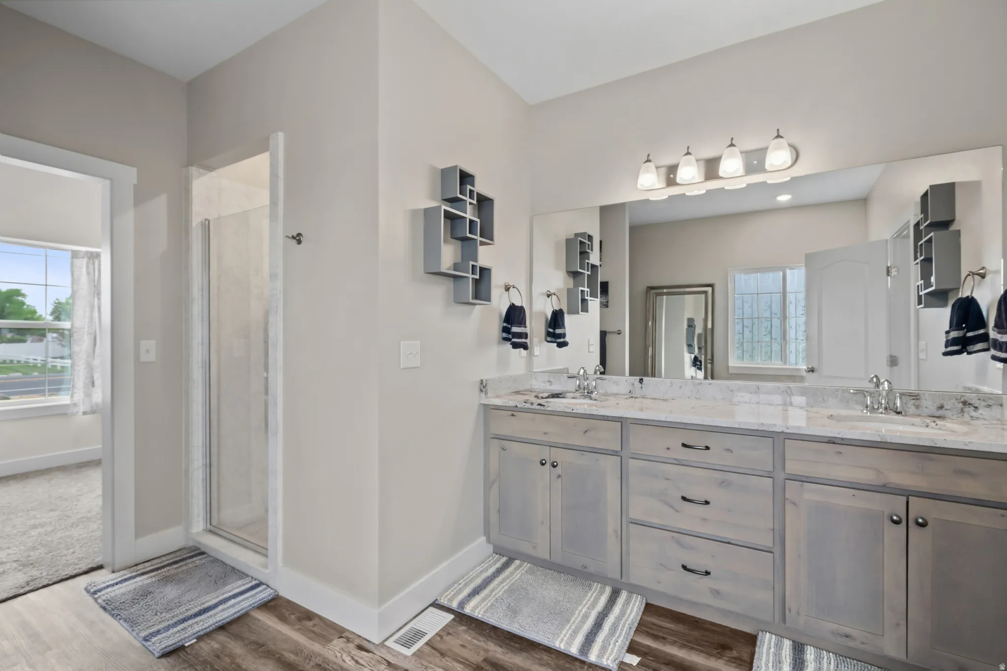 Full bath with double vanity, a shower stall, and dark wood finished floors