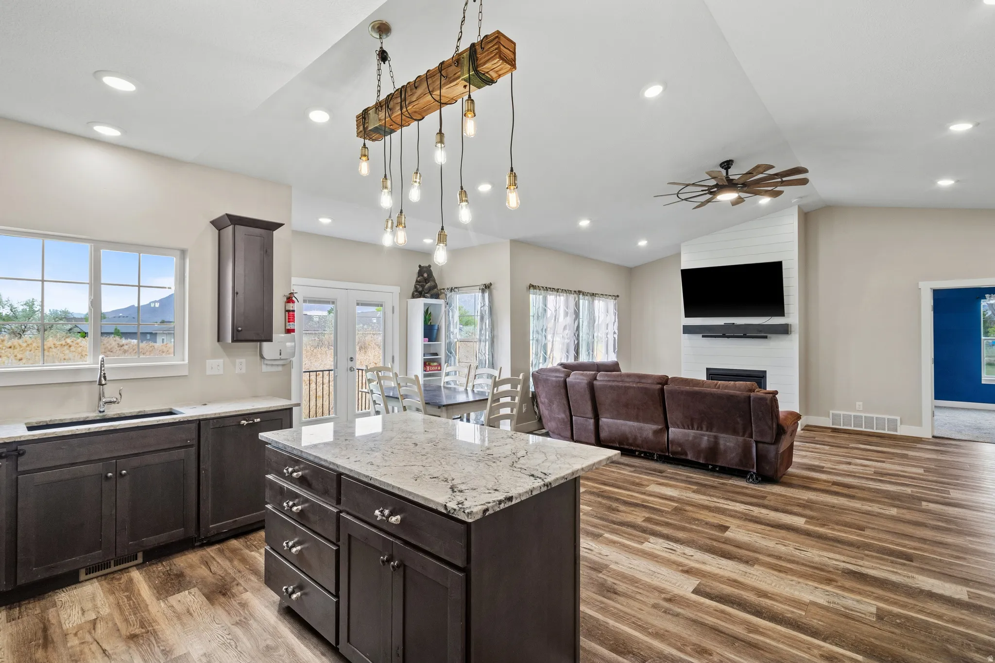 Kitchen featuring a center island, dark wood finish cabinets, light wood-style flooring, light stone counters, and lofted ceiling