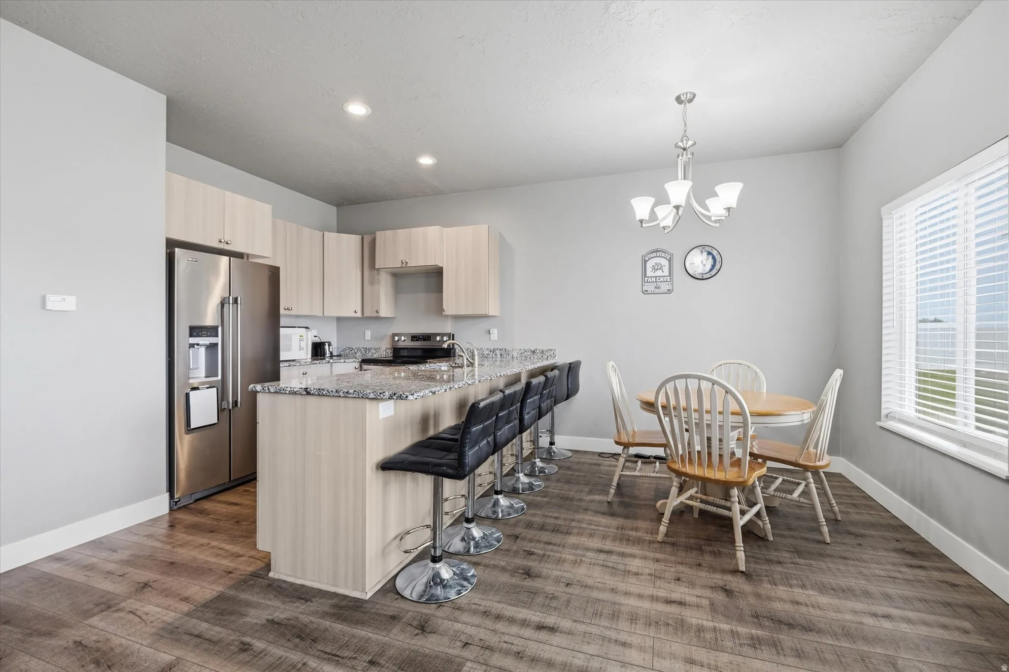 Kitchen featuring light stone counters, light wood finish cabinetry, stainless steel appliances, a peninsula, and suspended lighting