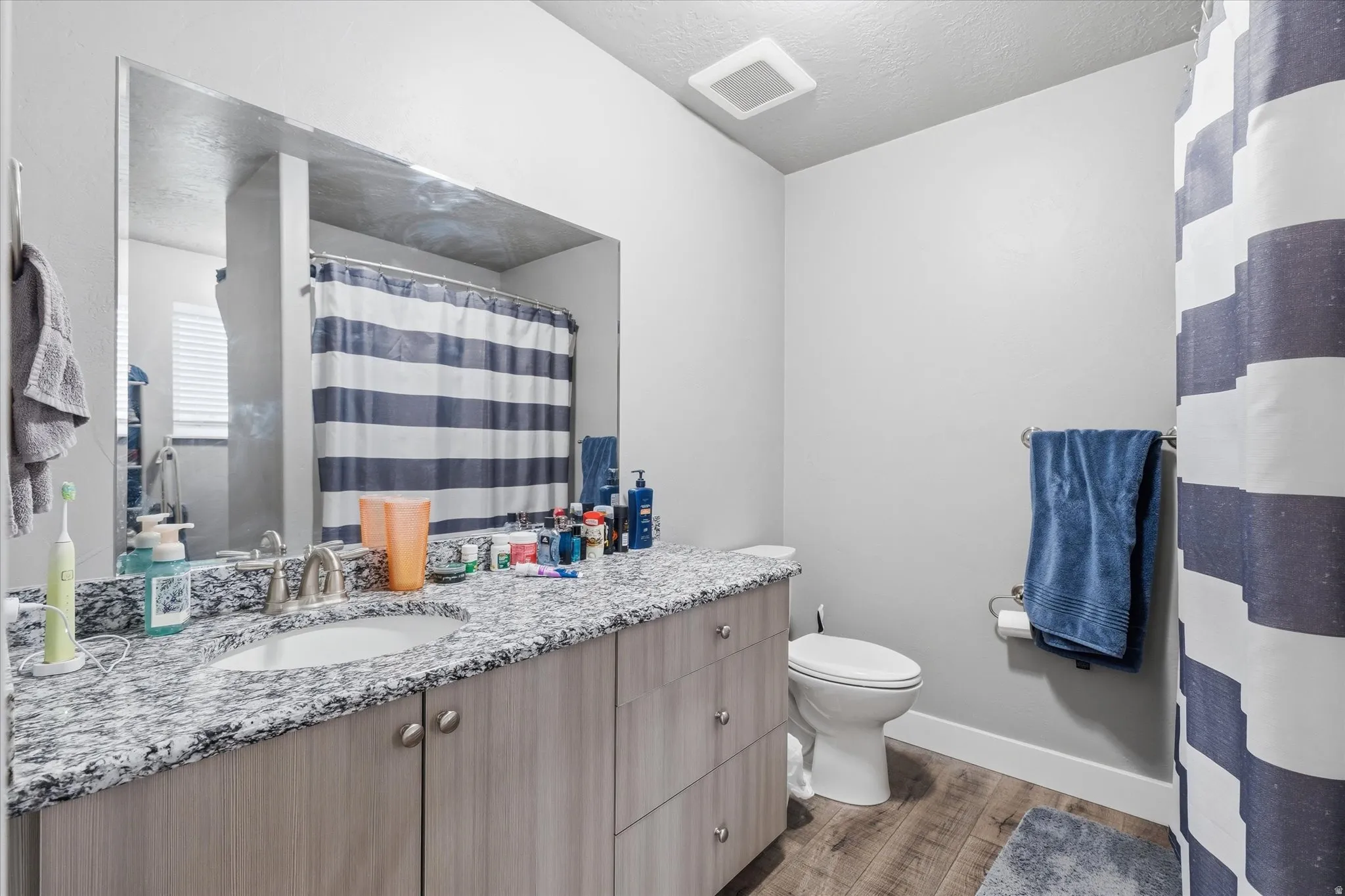 Full bath featuring vanity, a shower with curtain, light wood-style flooring, and a textured ceiling