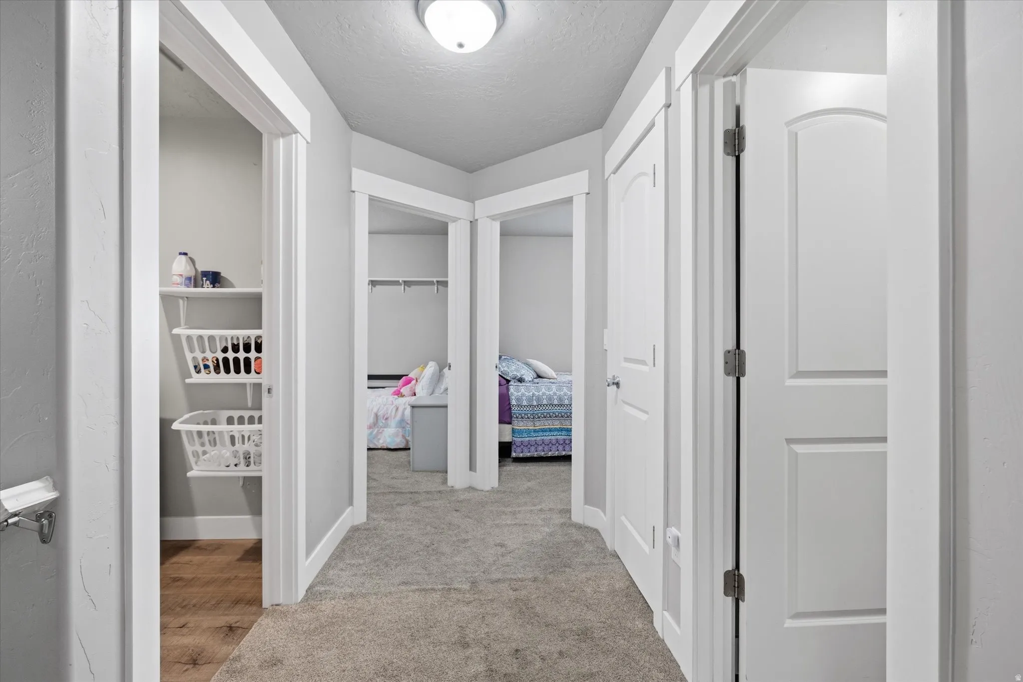 Corridor with a textured ceiling, light colored carpet, and light wood-style floors
