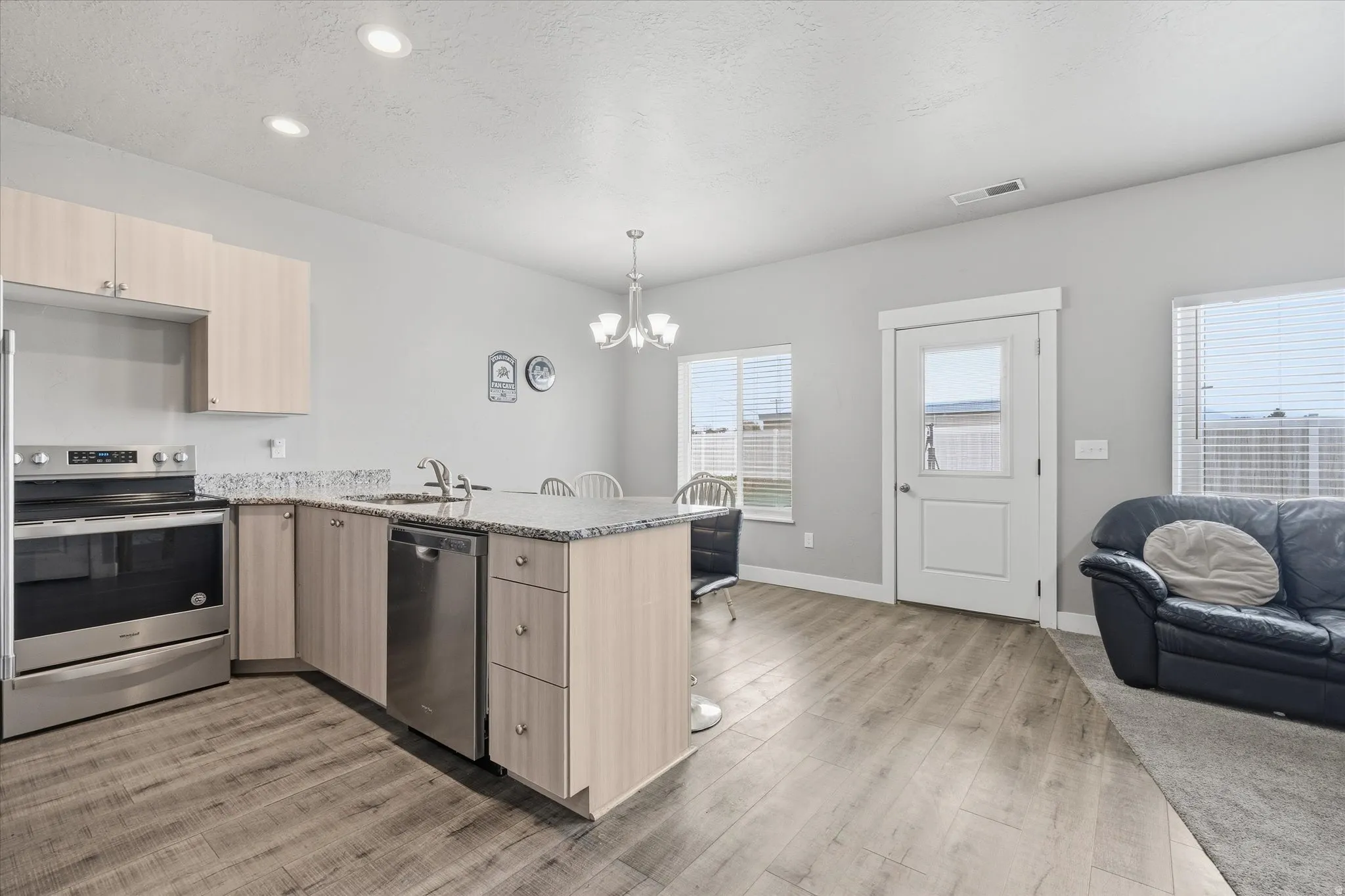 Kitchen with light wood finish cabinets, a peninsula, stainless steel appliances, light stone counters, and hanging lights
