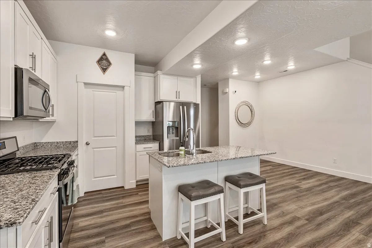 Kitchen featuring stainless steel appliances, a center island with sink, light stone countertops, white cabinets, and a breakfast bar area