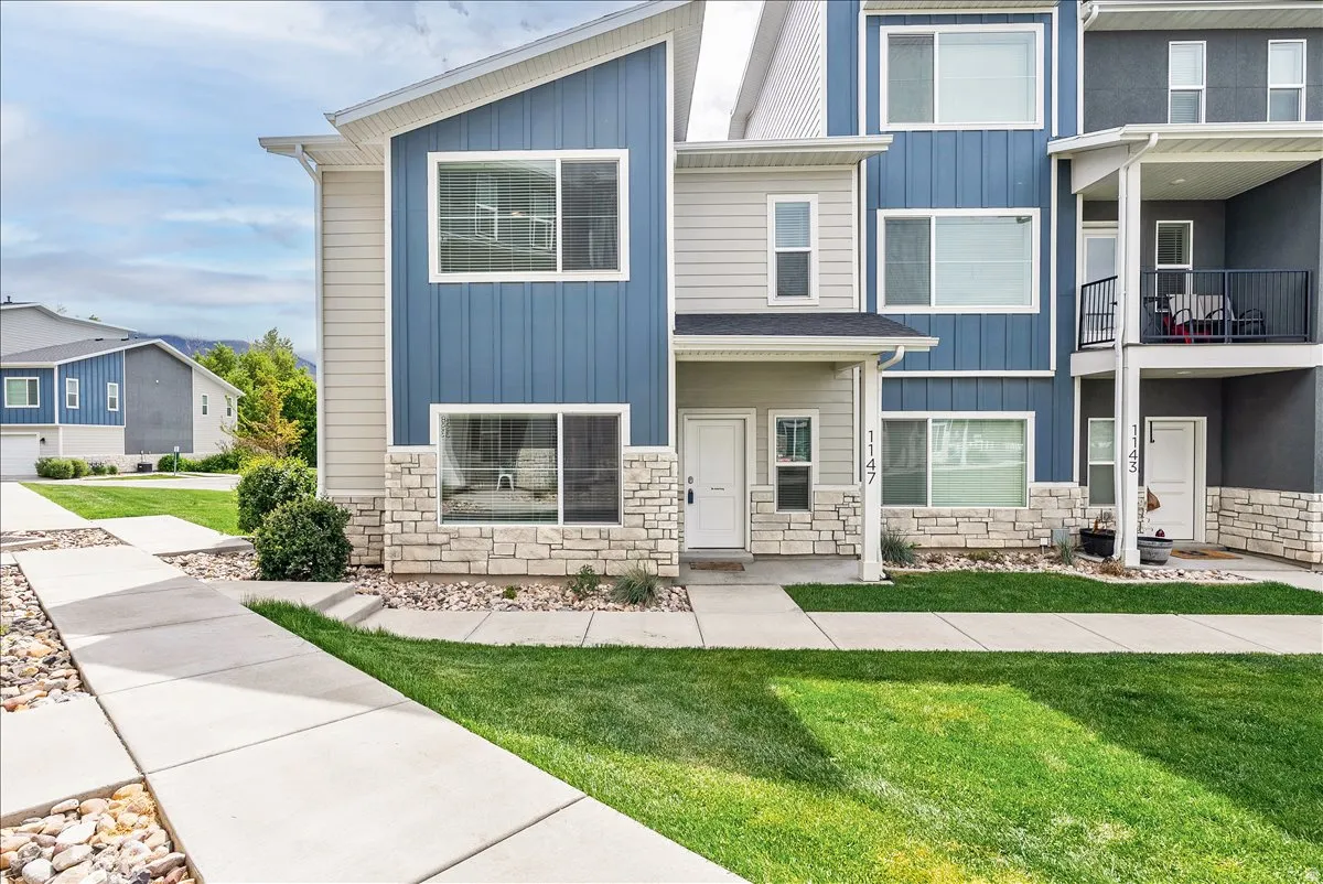 View of front of house with board and batten siding, stone siding, a front yard, and a balcony