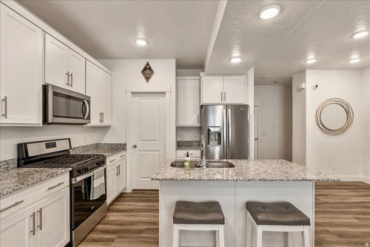 Kitchen featuring stainless steel appliances, light wood-style flooring, white cabinetry, light stone counters, and recessed lighting