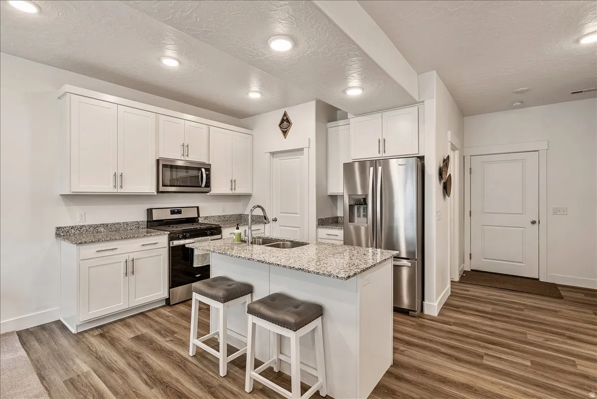 Kitchen with stainless steel appliances, light stone counters, white cabinets, a kitchen breakfast bar, and a center island with sink