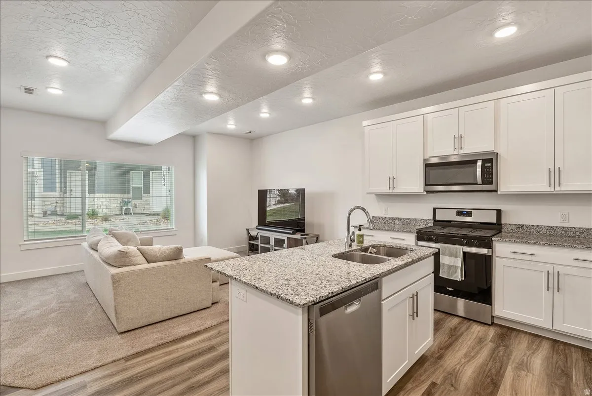 Kitchen with stainless steel appliances, open floor plan, light stone countertops, white cabinets, and a kitchen island with sink