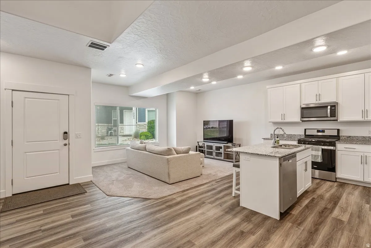 Kitchen featuring open floor plan, stainless steel appliances, a kitchen bar, white cabinets, and a textured ceiling