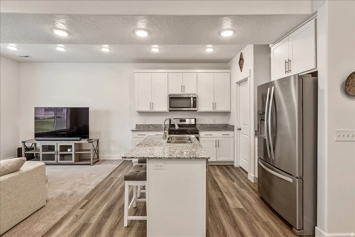 Kitchen featuring stainless steel appliances, open floor plan, light stone counters, white cabinets, and a kitchen island with sink