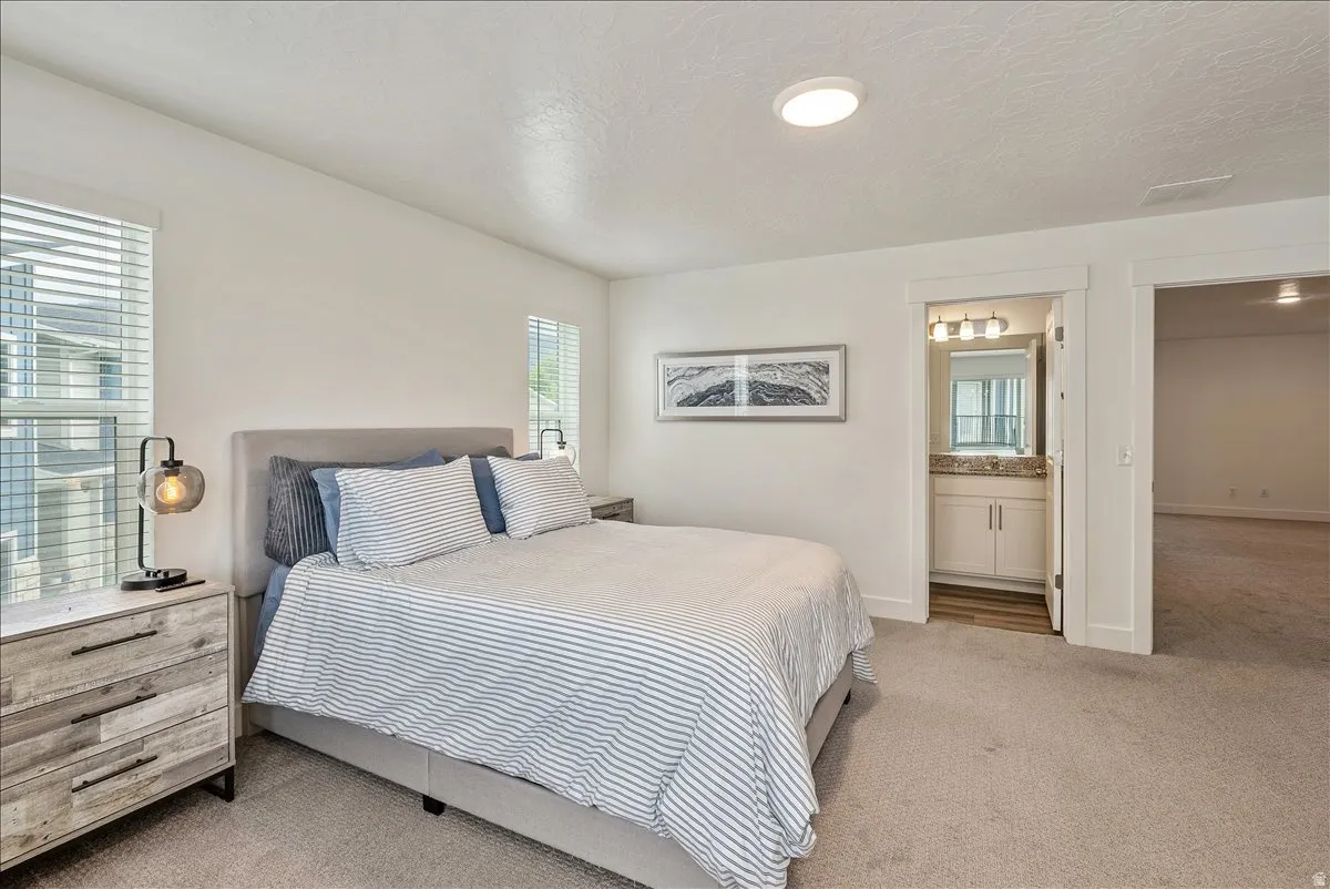 Carpeted bedroom featuring multiple windows, a textured ceiling, and ensuite bathroom