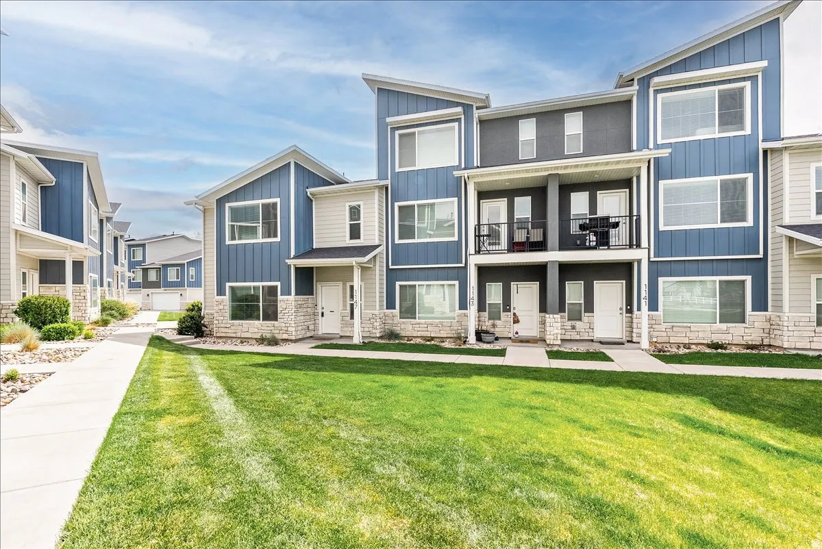 View of front of house featuring stone siding, board and batten siding, a front lawn, and a balcony