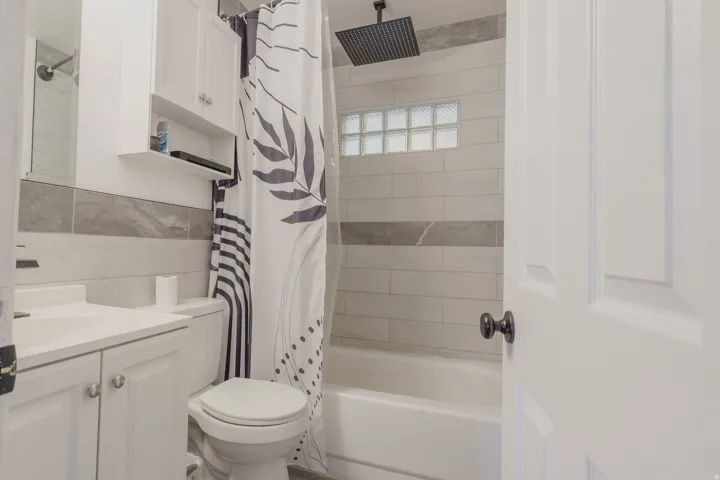 Modern bathroom featuring white cabinetry, a single basin vanity, a toilet, a shower/tub combination with tile surround, and a ceiling-mounted rainfall showerhead