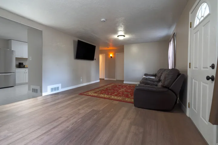 Wood-finish flooring, a white paneled entry door with an arched glass insert, and a kitchen featuring stainless steel appliances and white cabinetry