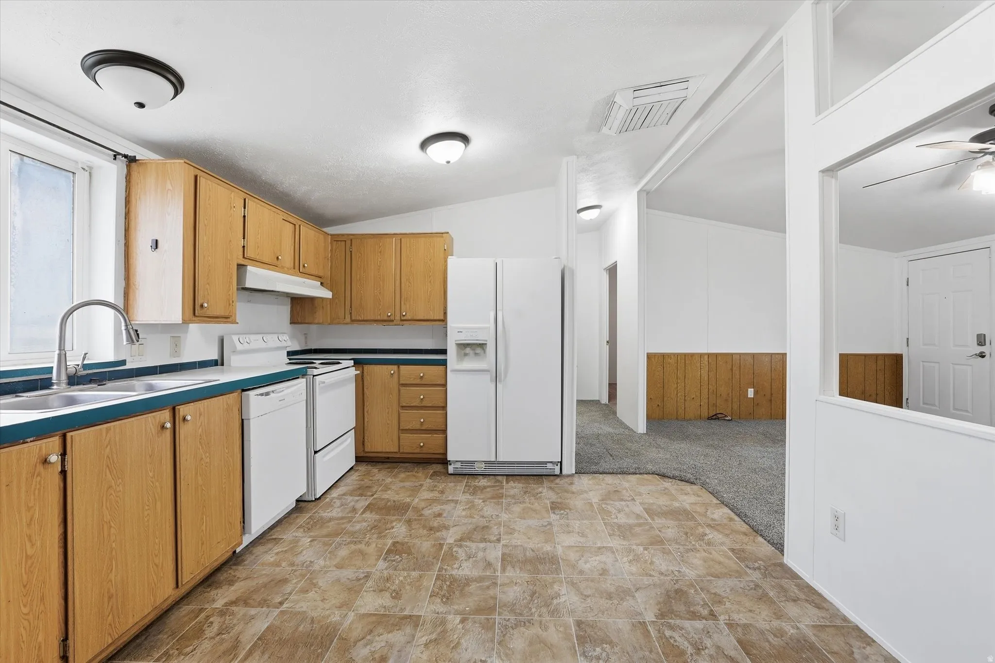 Kitchen with light carpet, white appliances, wooden walls, lofted ceiling, and wood finish cabinets