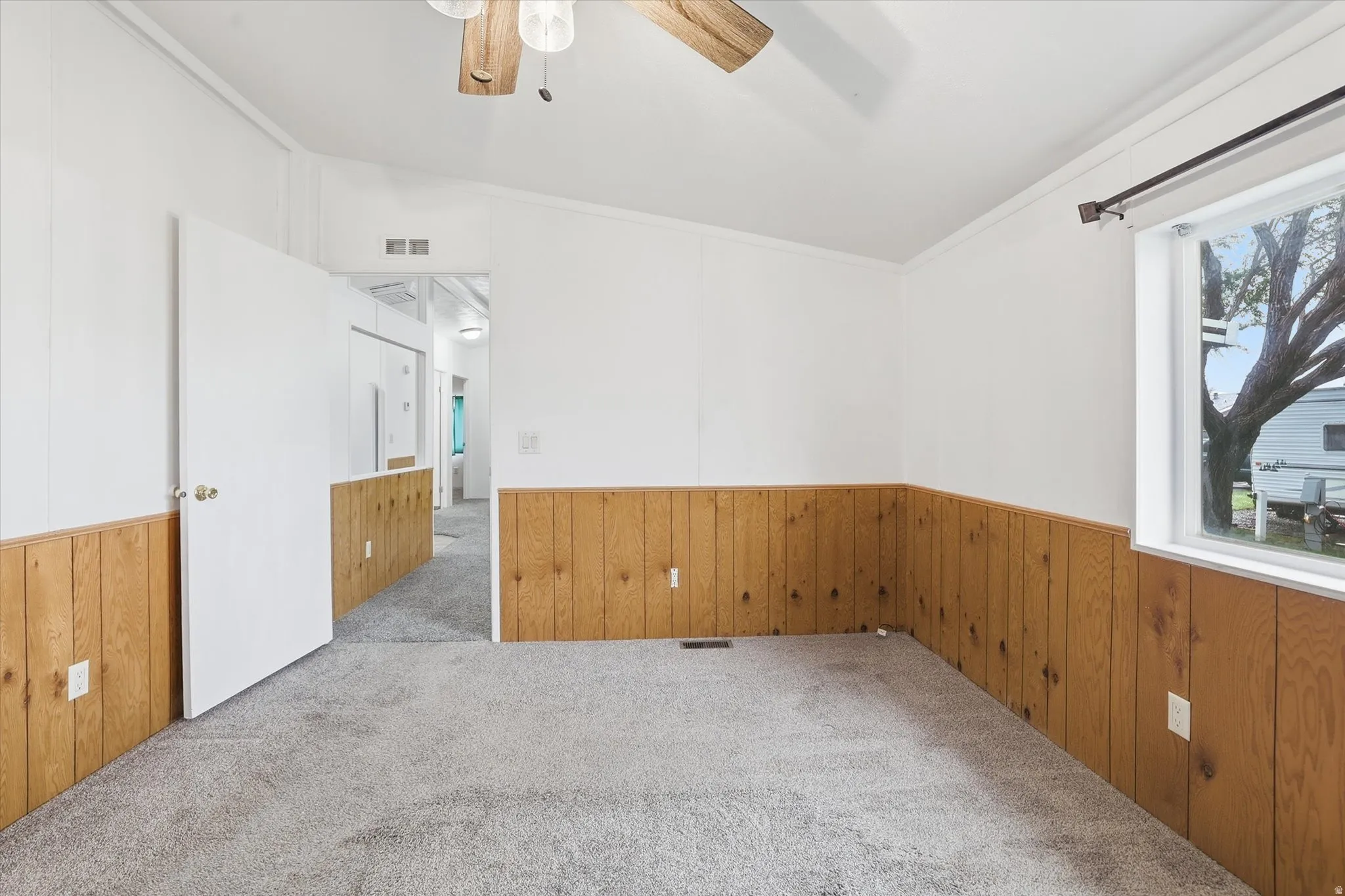 Empty room featuring wood walls, carpet flooring, ornamental molding, wainscoting, and ceiling fan