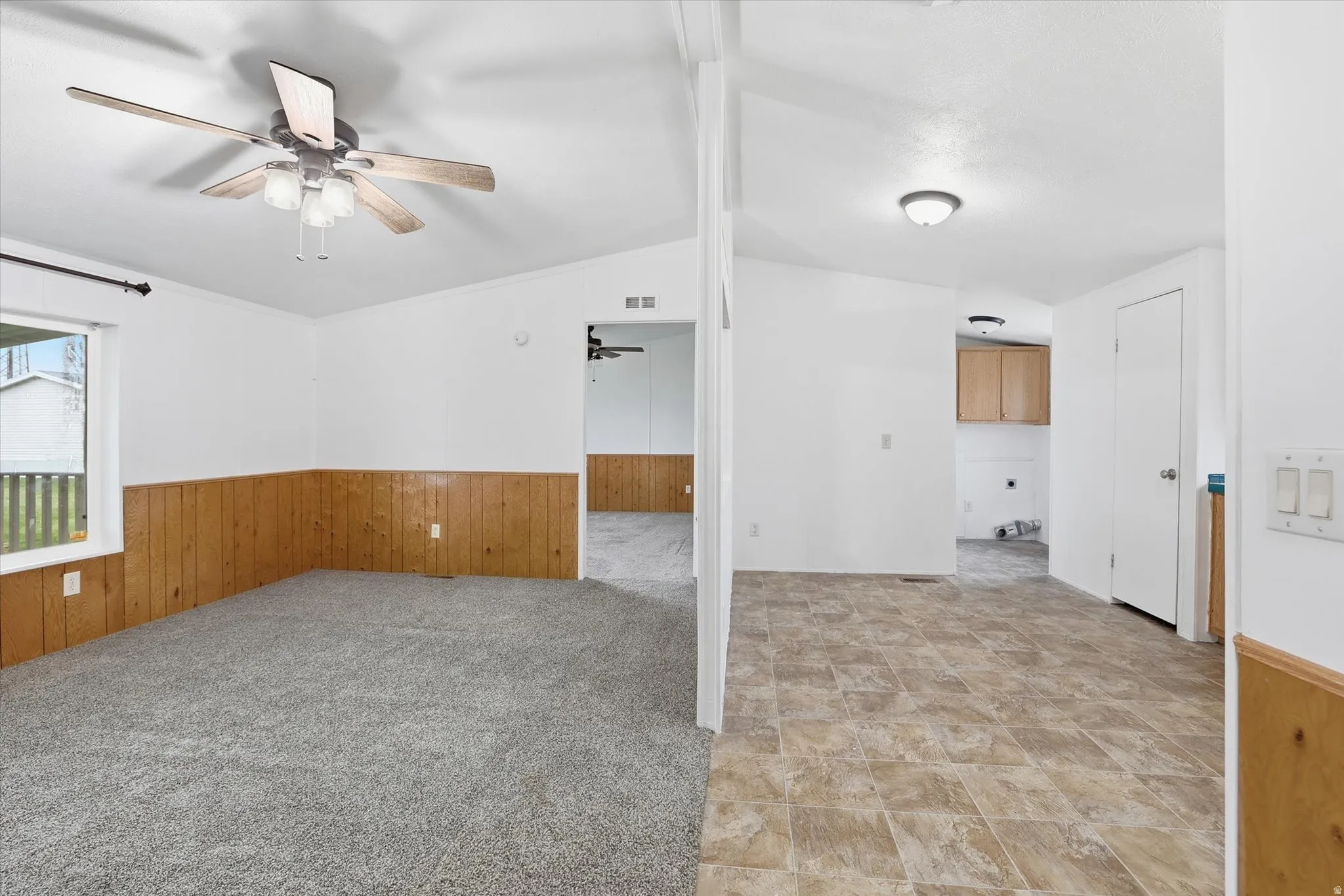 Unfurnished room with light colored carpet, wooden walls, wainscoting, vaulted ceiling, and ceiling fan